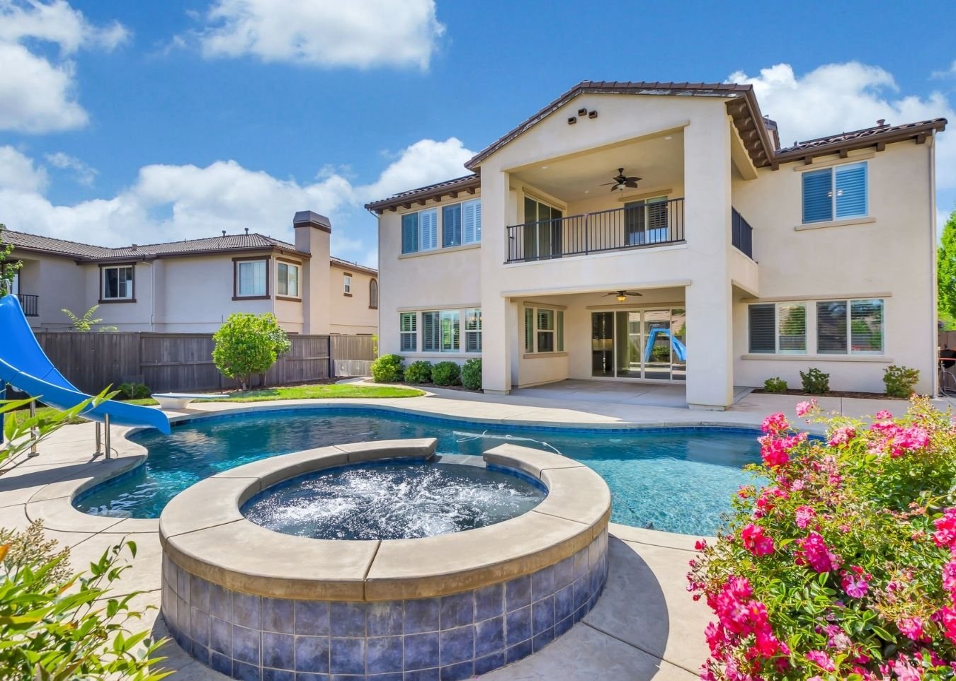 Luxury backyard with resort-style swimming pool, stone waterfall features, tropical landscaping, and lounge seating at sunset in an upscale California home.