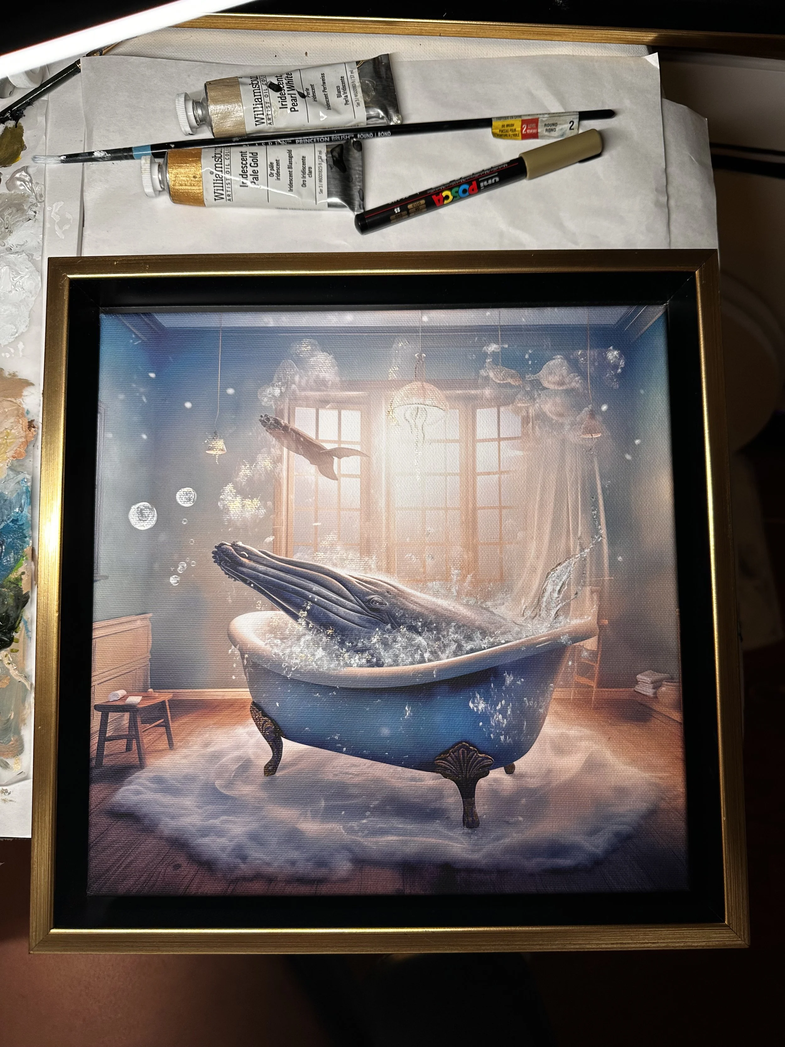 MADX Magic Whale Tub surreal fine art canvas print in gold float frame with artist paints and brushes. Limited edition mixed-media artwork showing humpback whale emerging from clawfoot bathtub by NYC artist MADX, being hand-embellished in studio.
