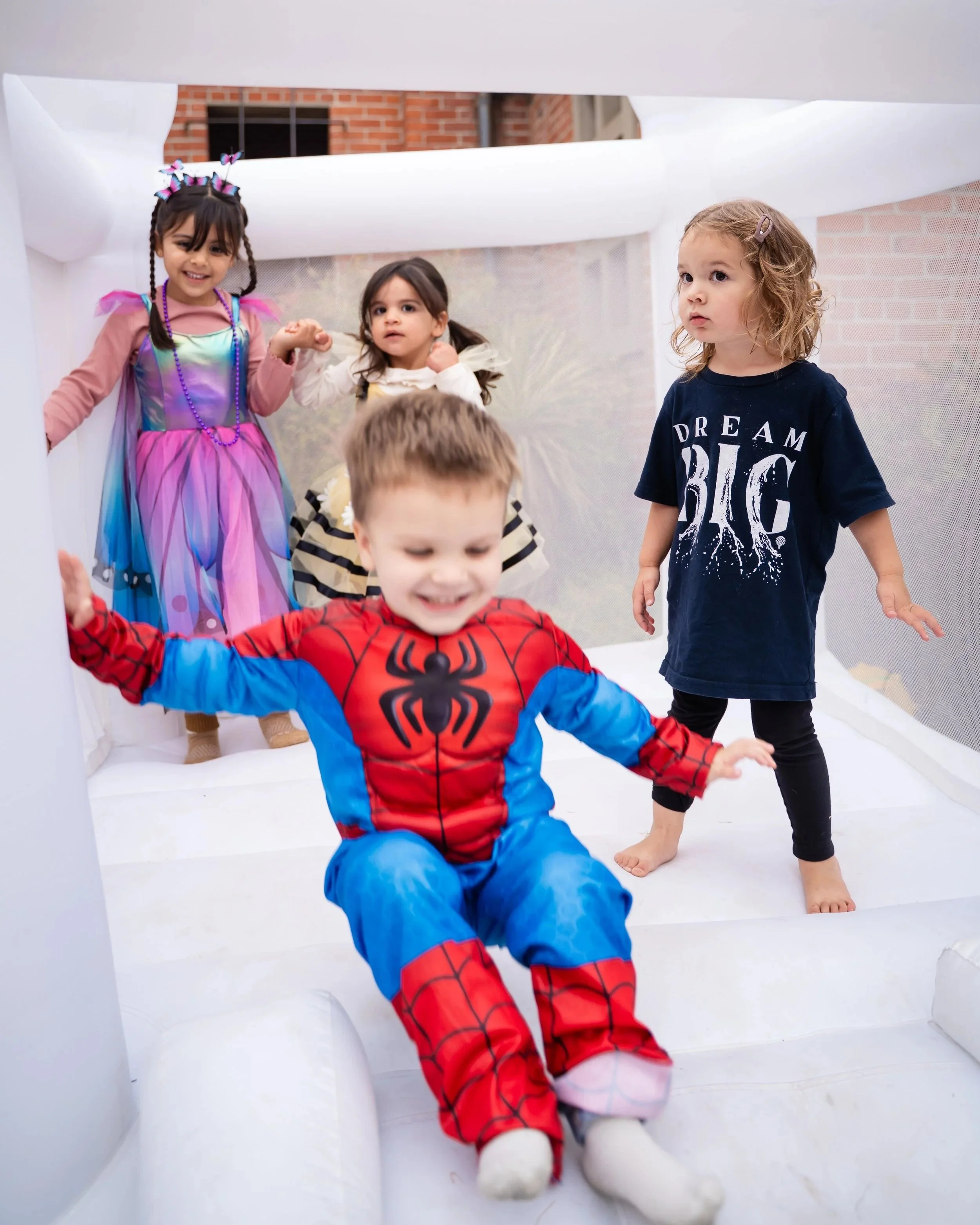 Group of children playing on an indoor inflatable bounce house or slide, with a brick building visible outside.