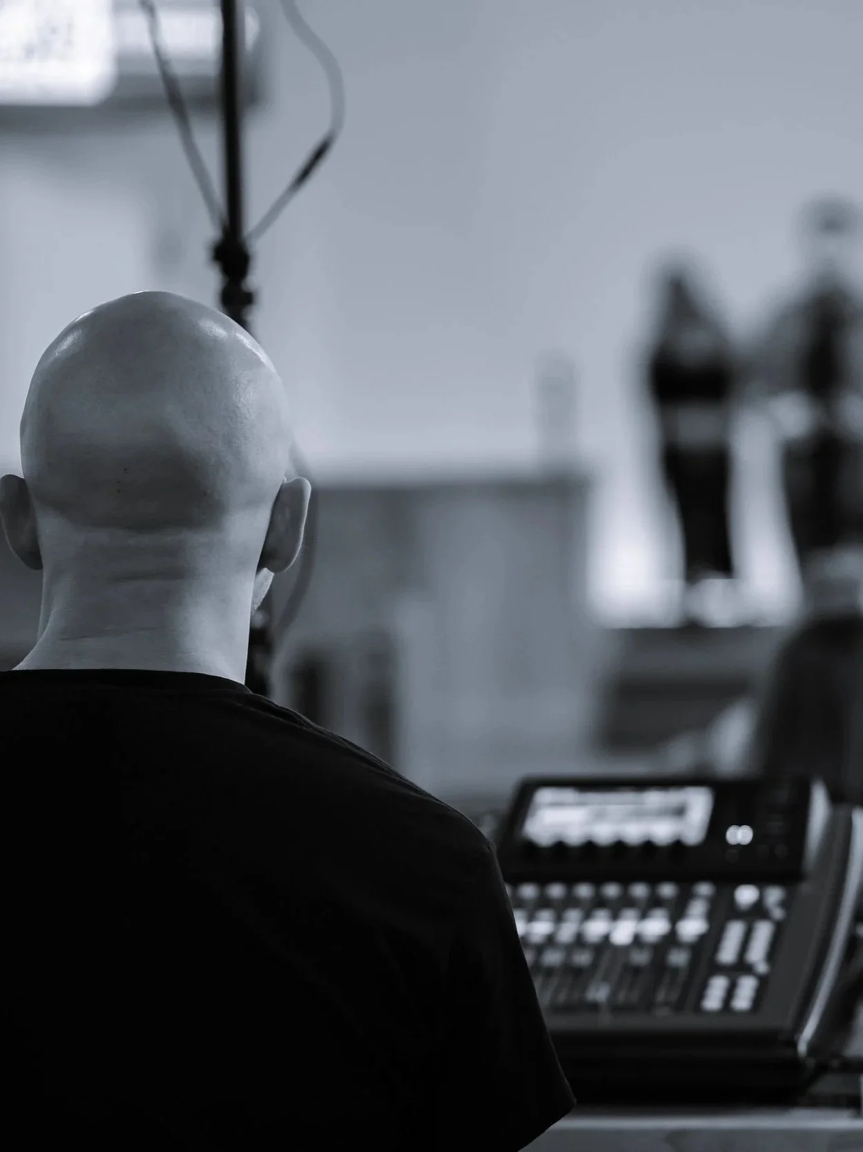Back of bald person sitting in front of sound mixing console in studio.
