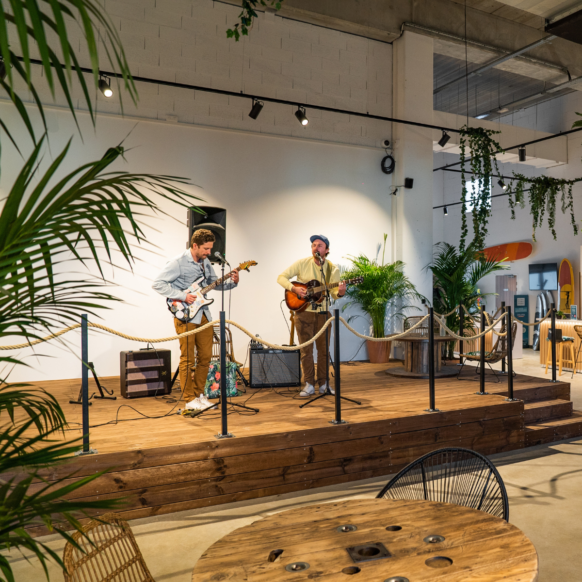 Deux musiciens jouent de la musique sur une scène en bois dans un espace intérieur décoré de plantes