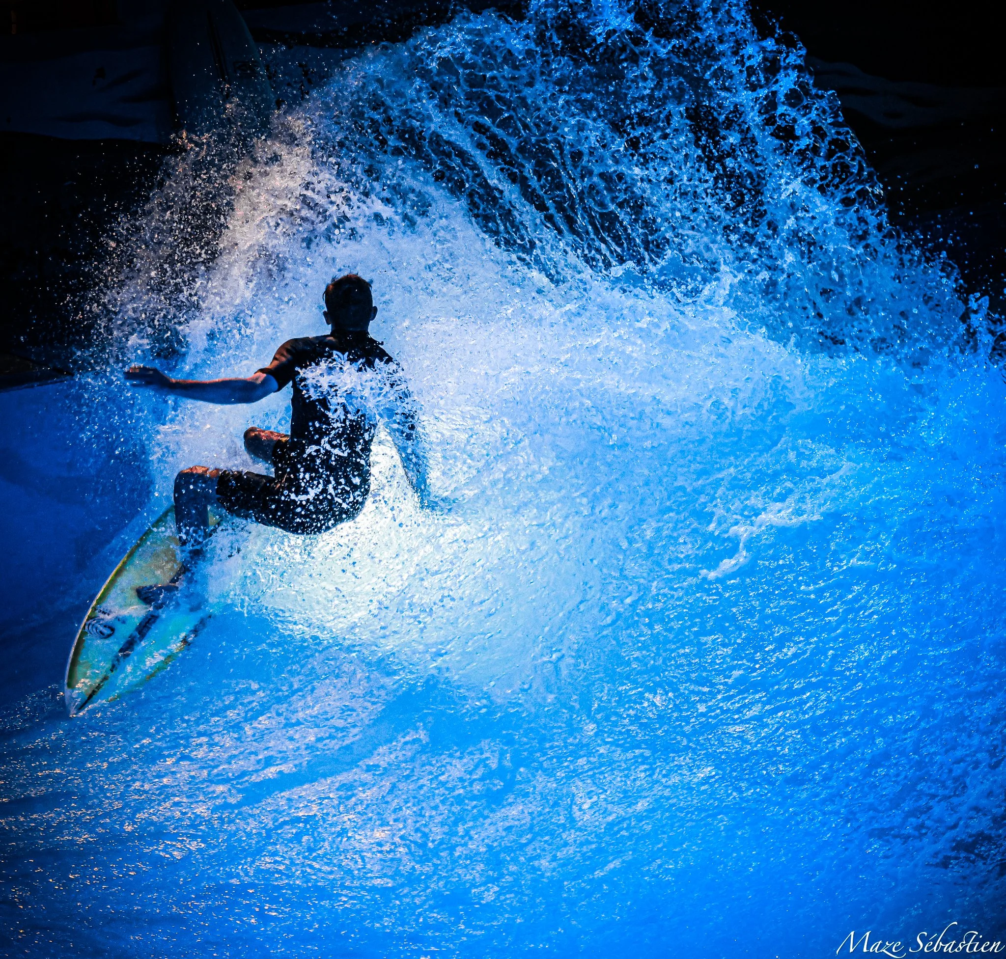 Un enfant fait du surf dans une vague bleue lumineuse, vu de dos.