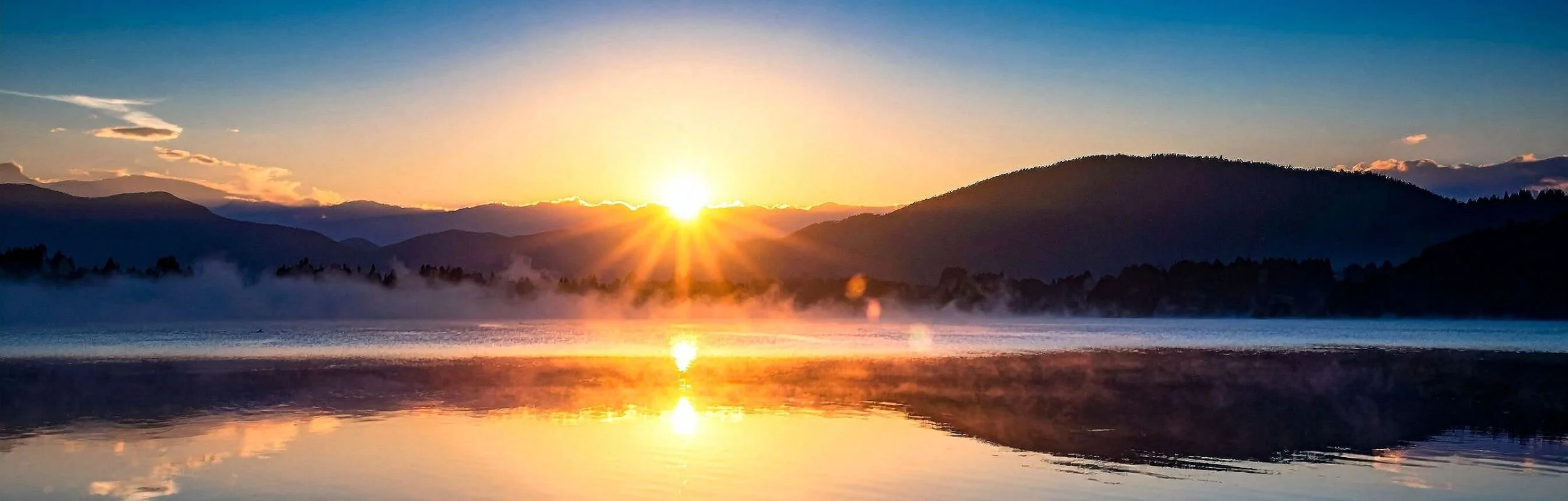 Holy Spirit Healing. Exorcist. Sunset over a mountain lake with mist rising from the water and a clear reflection of the sky and mountains on the lake's surface.