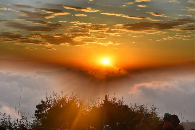 Christ Consciousness. Sunset over a mountain with clouds and silhouettes of trees and people in the foreground.