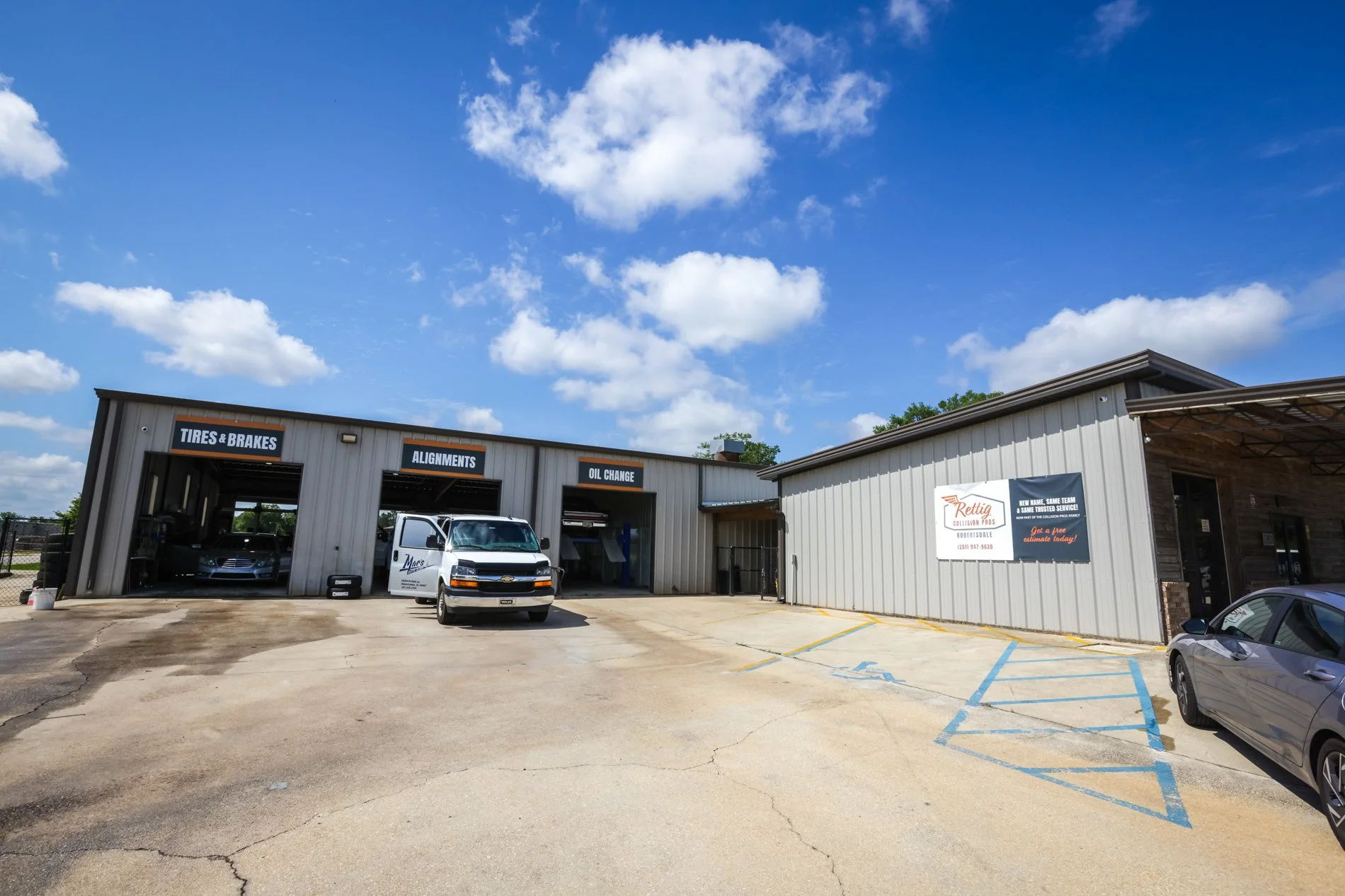 Exterior view of an auto repair shop with three service bays labeled tires & brakes, alignments, and oil change. A white van with a company logo is parked in front, and there are a few cars in the parking lot under a sunny sky with scattered clouds.