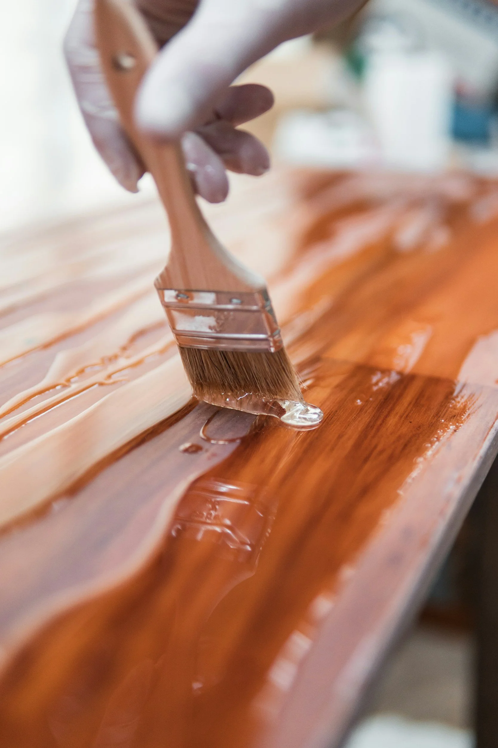 A person applying a clear finish to wood using a paintbrush, with wood grains visible underneath.
