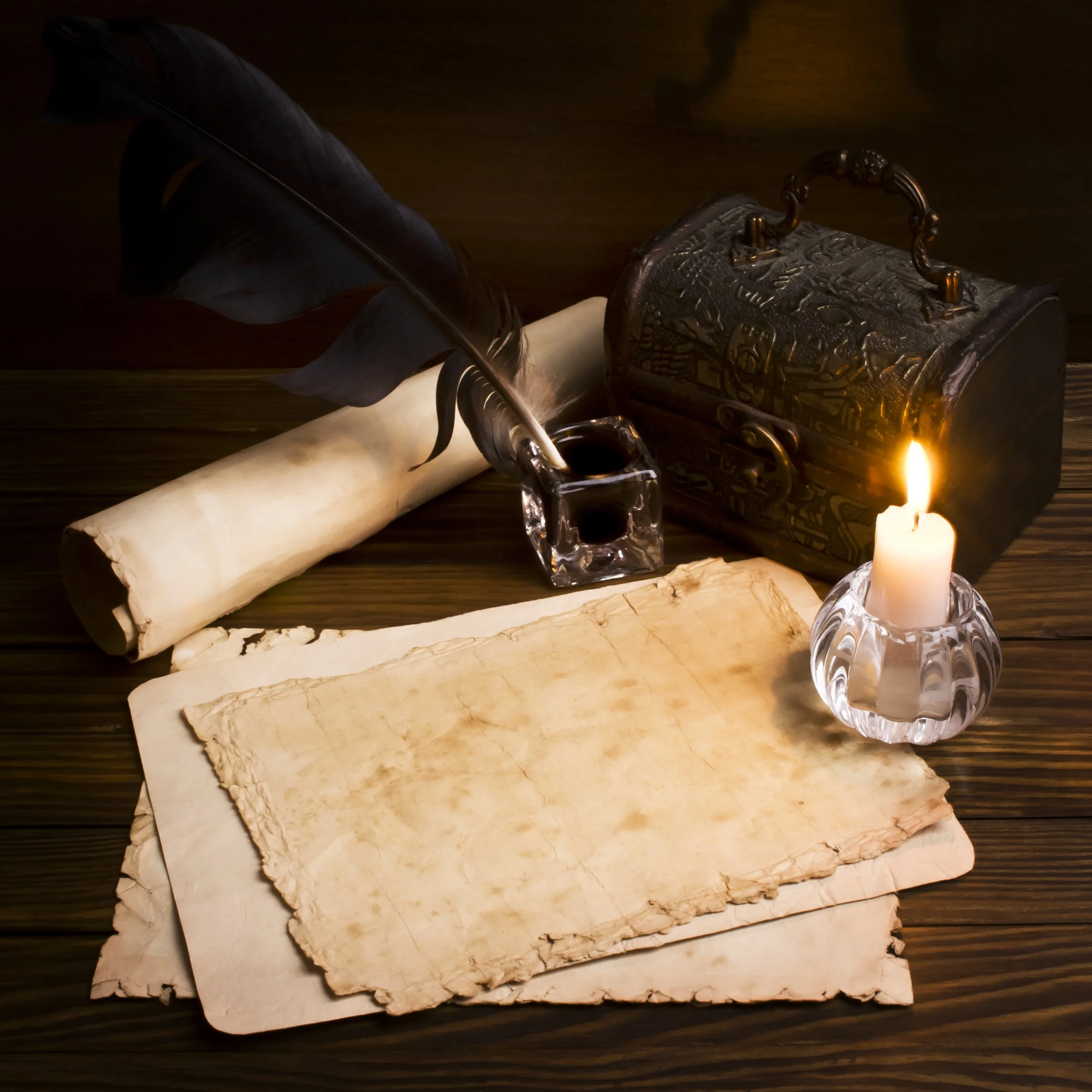 A quill pen in ink bottle, old parchment papers, a scroll, a lit candle, a small ornate box, and a torch with a wooden background.