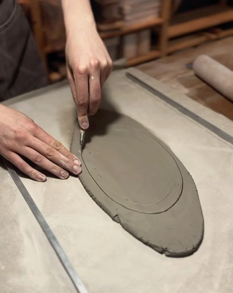 Manos trabajando una plancha de arcilla sobre una mesa de cerámica.