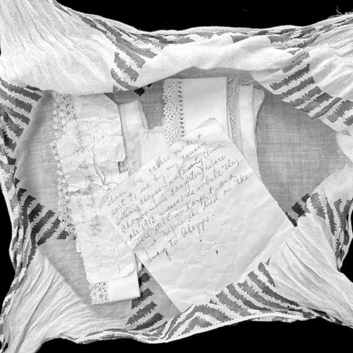 Black and white photo of a handwritten note atop Armenian handwork