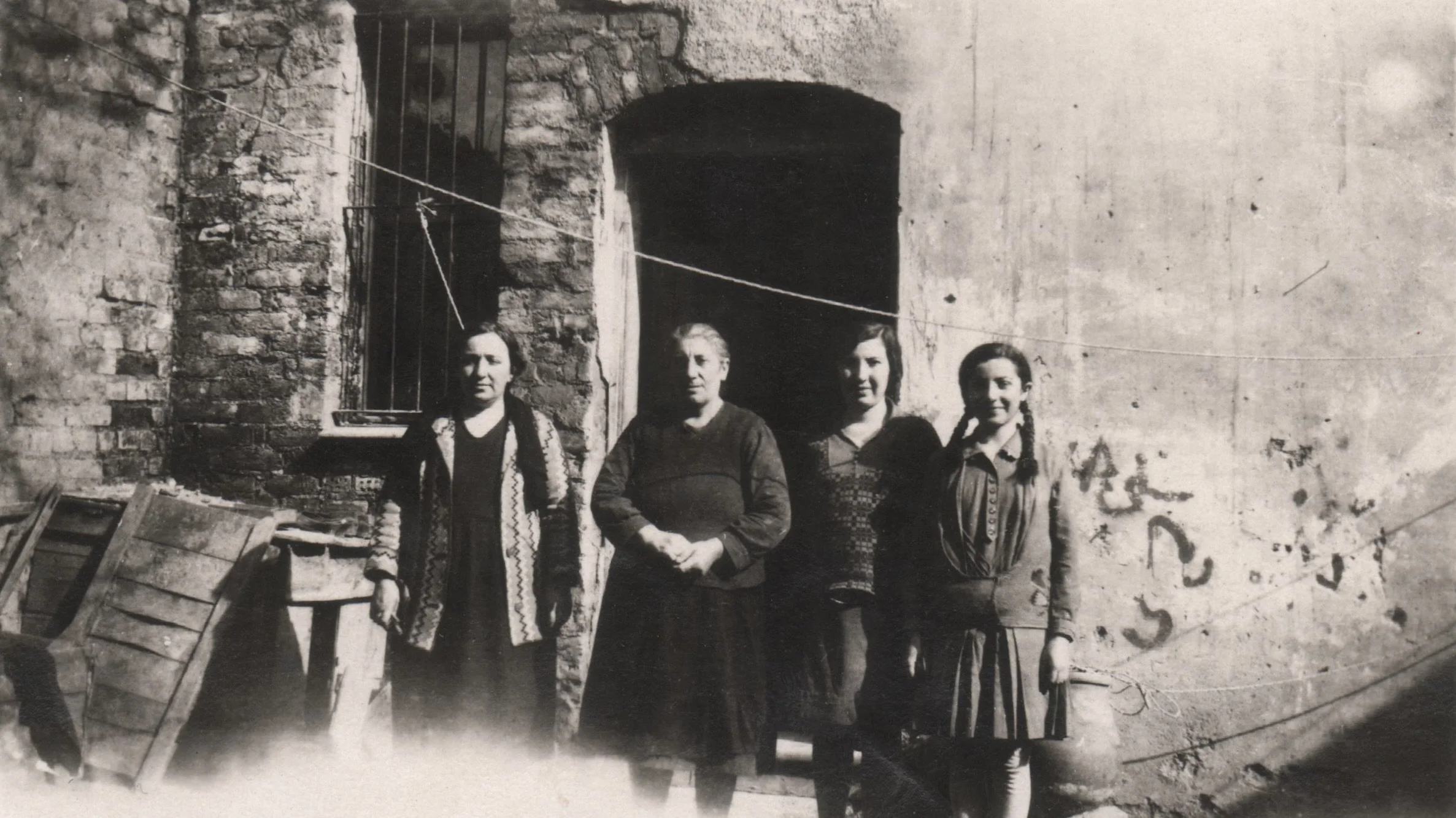 Black and white photo of four women standing together in front of a stone structure