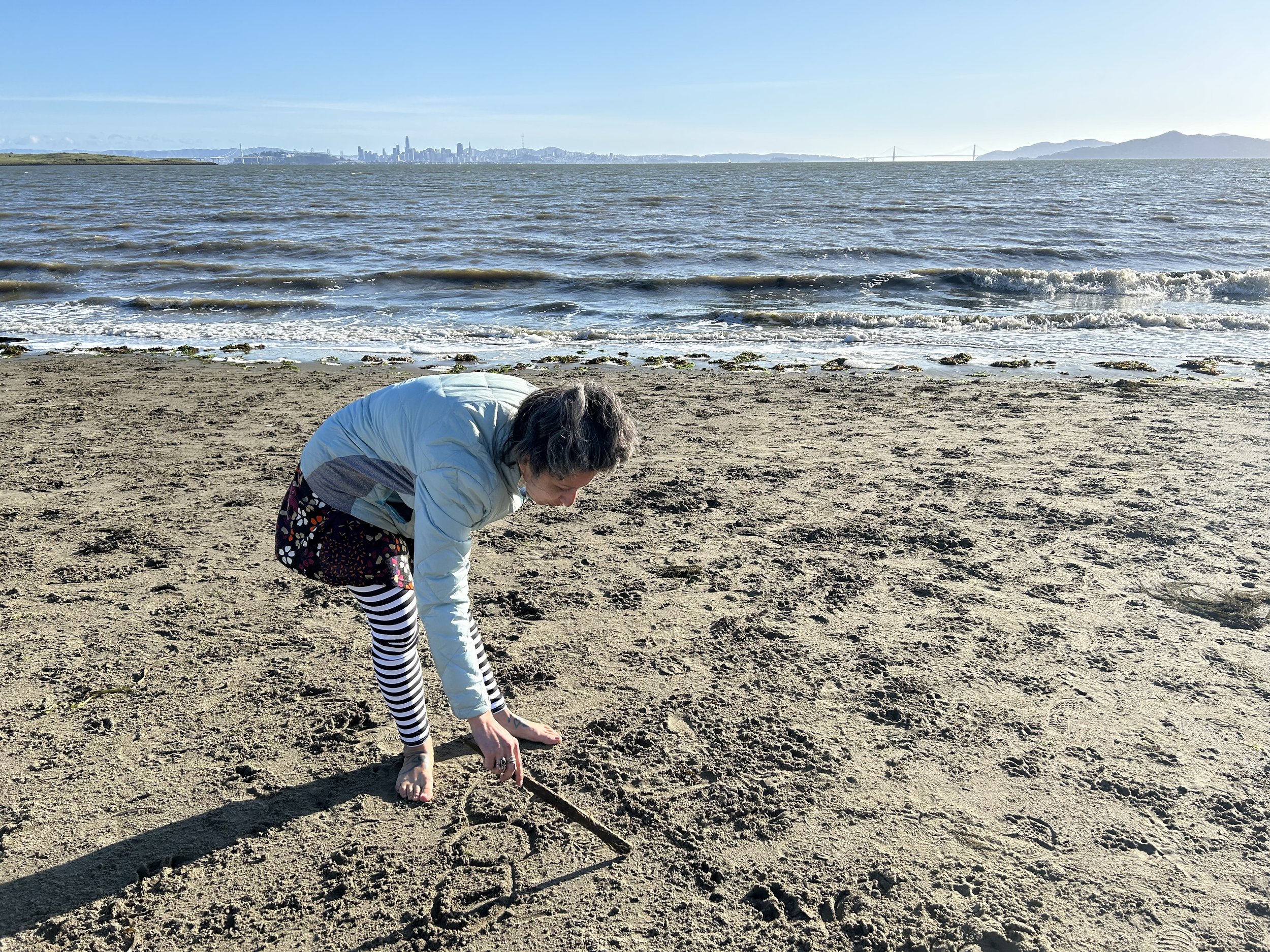 Elise Youssoufian drawing Armenian needlelace in the sand at a beach on the San Francisco Bay, 2024. Photograph by Deborah Valoma.
