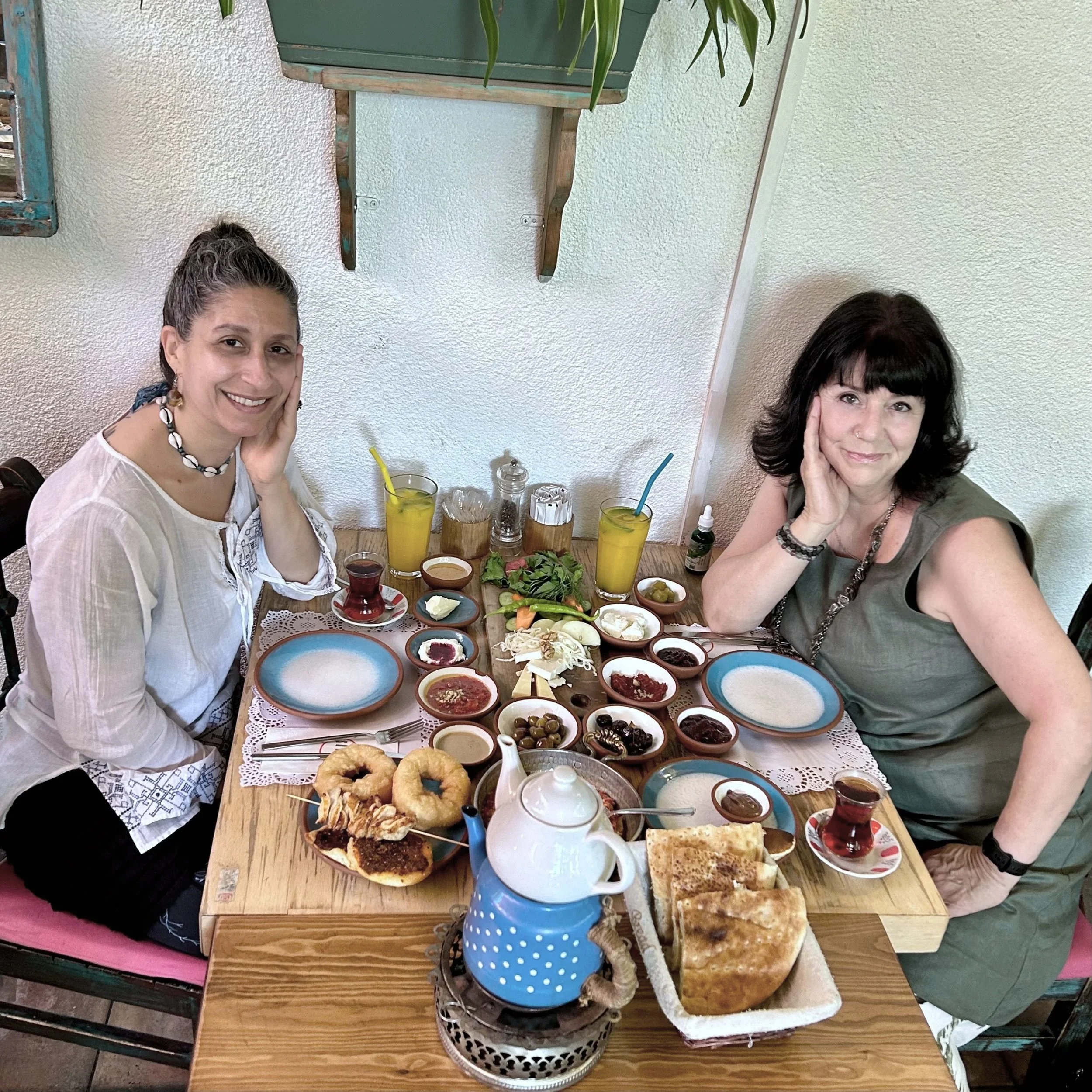 Colorful photo of Armenian Needlelace Initiative co-founders Elise Youssoufian, in white blouse, and Deborah Valoma, in olive green dress, having breakfast and smiling
