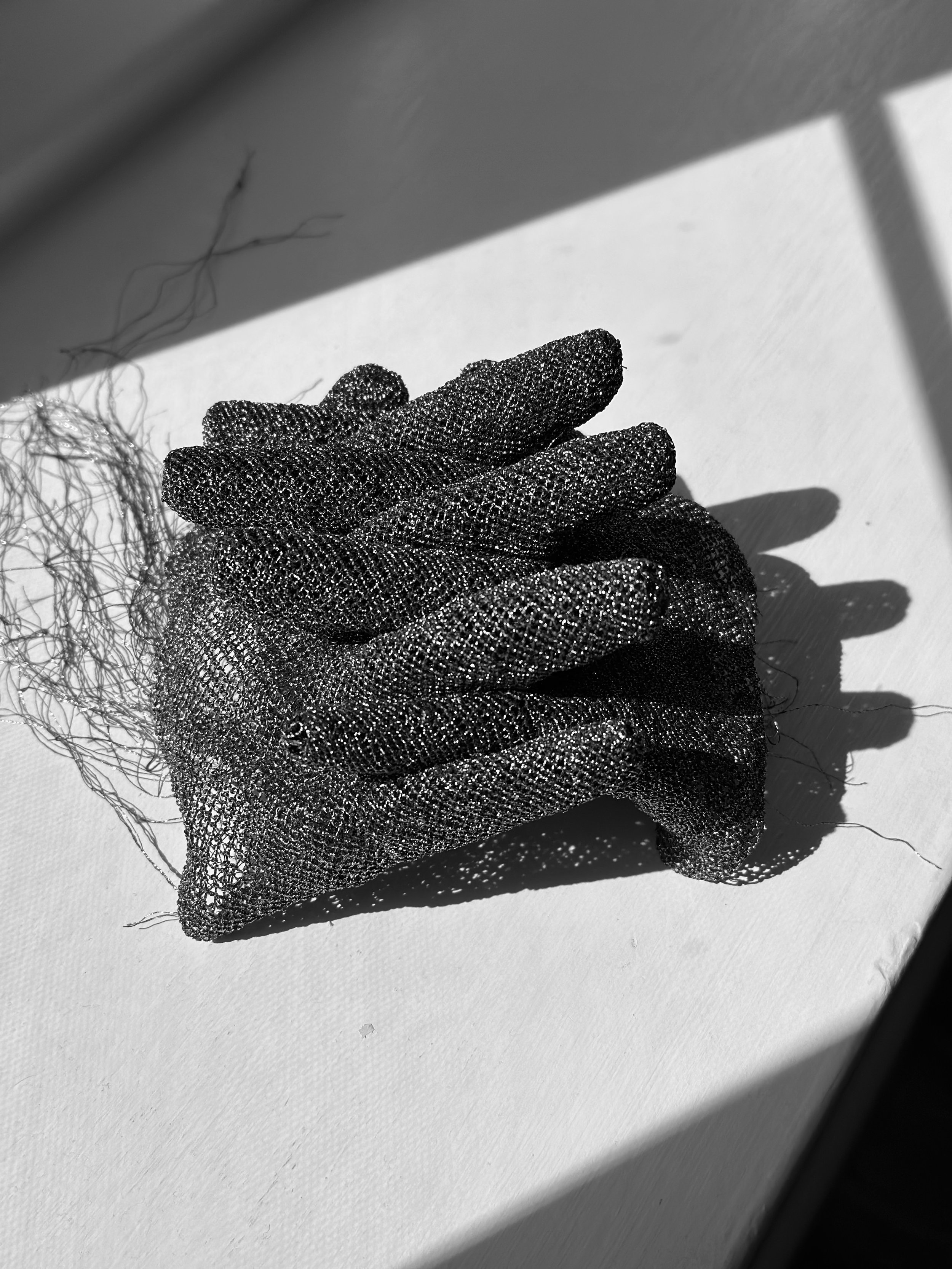 Black and white photograph of sculpture of fingers intertwined and loose threads