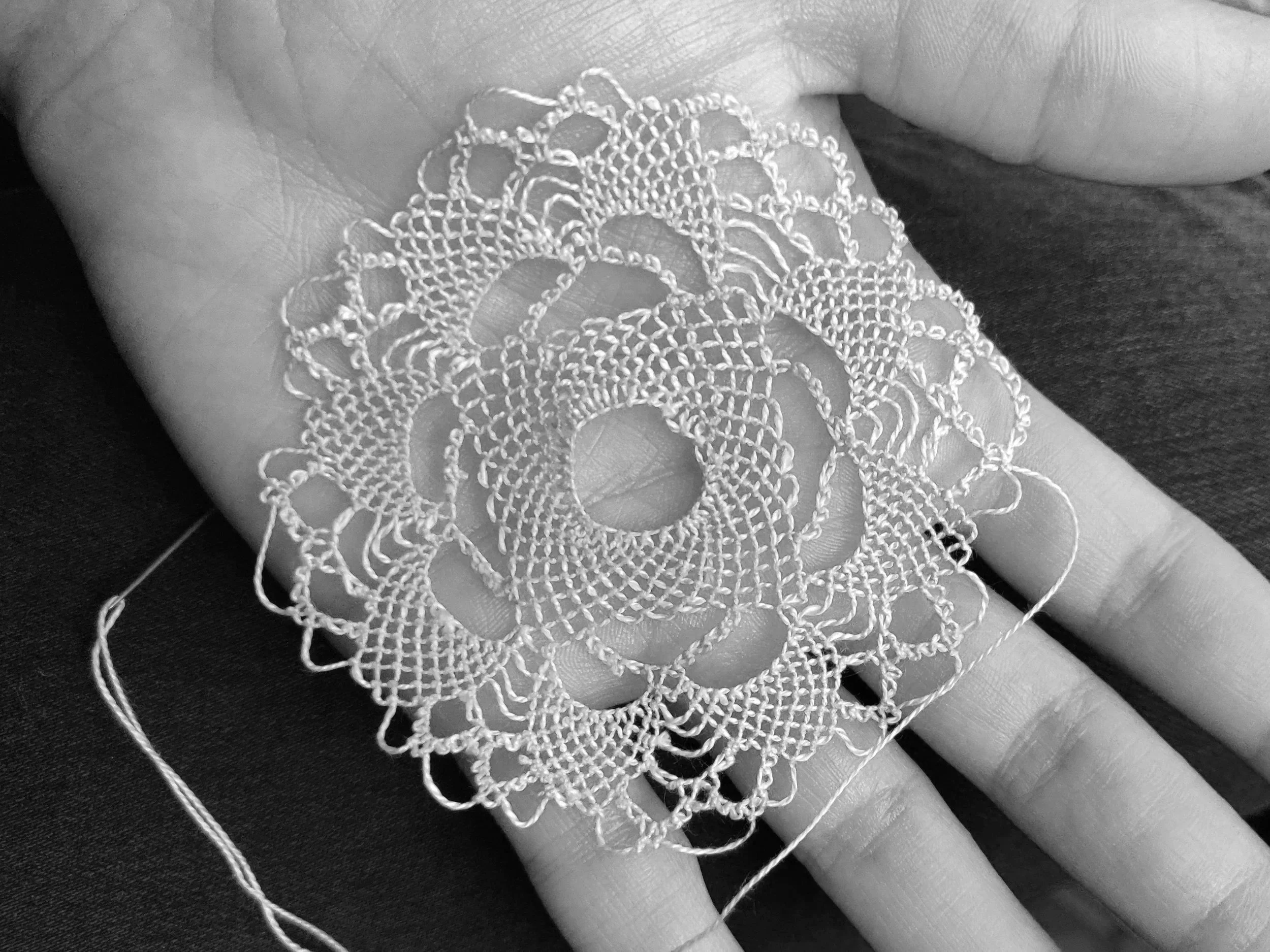 Black and white photo of Armenian needlelace medallion in progress, held in open hand