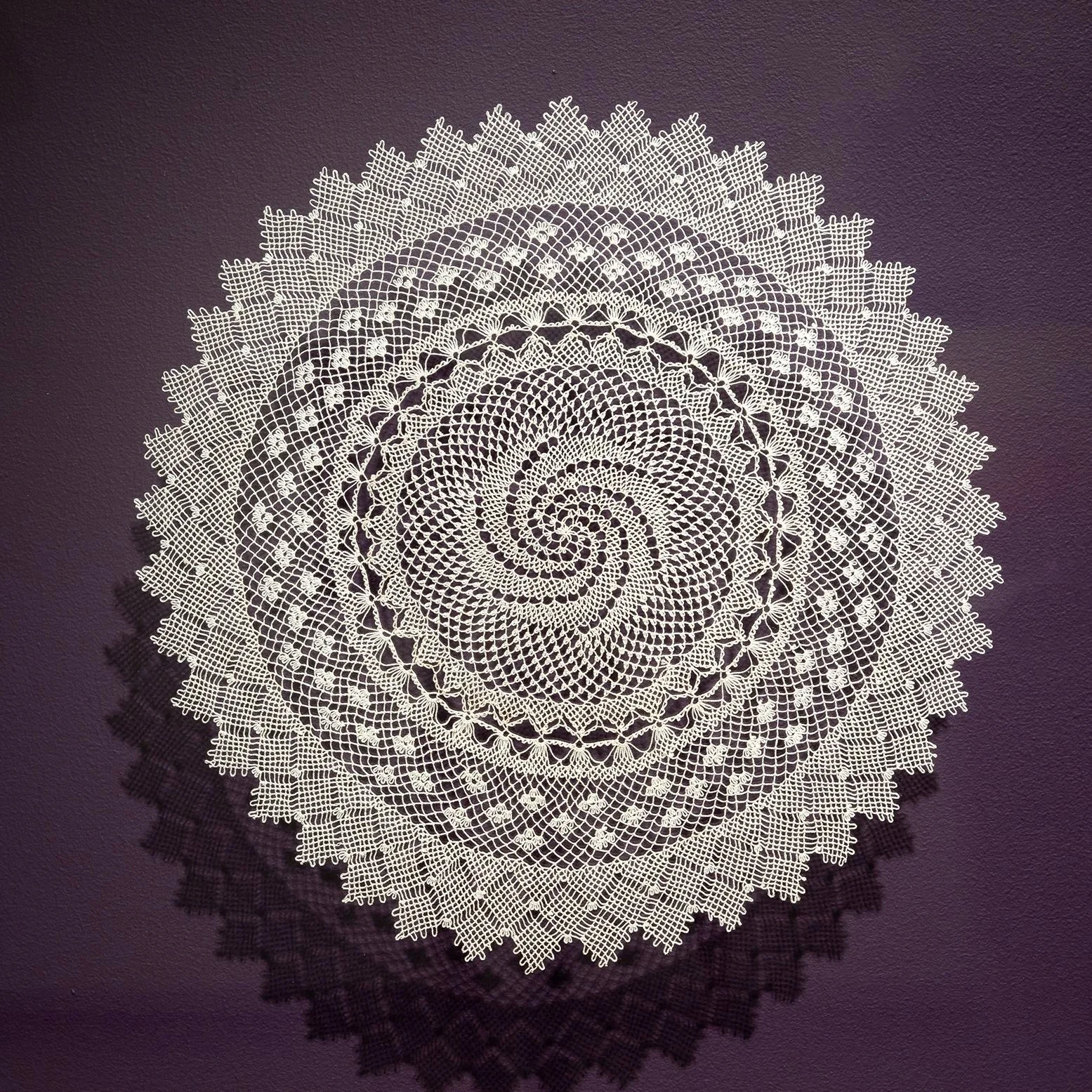 Color photo of off-white Armenian needlelace doily, with aubergine-tinted background