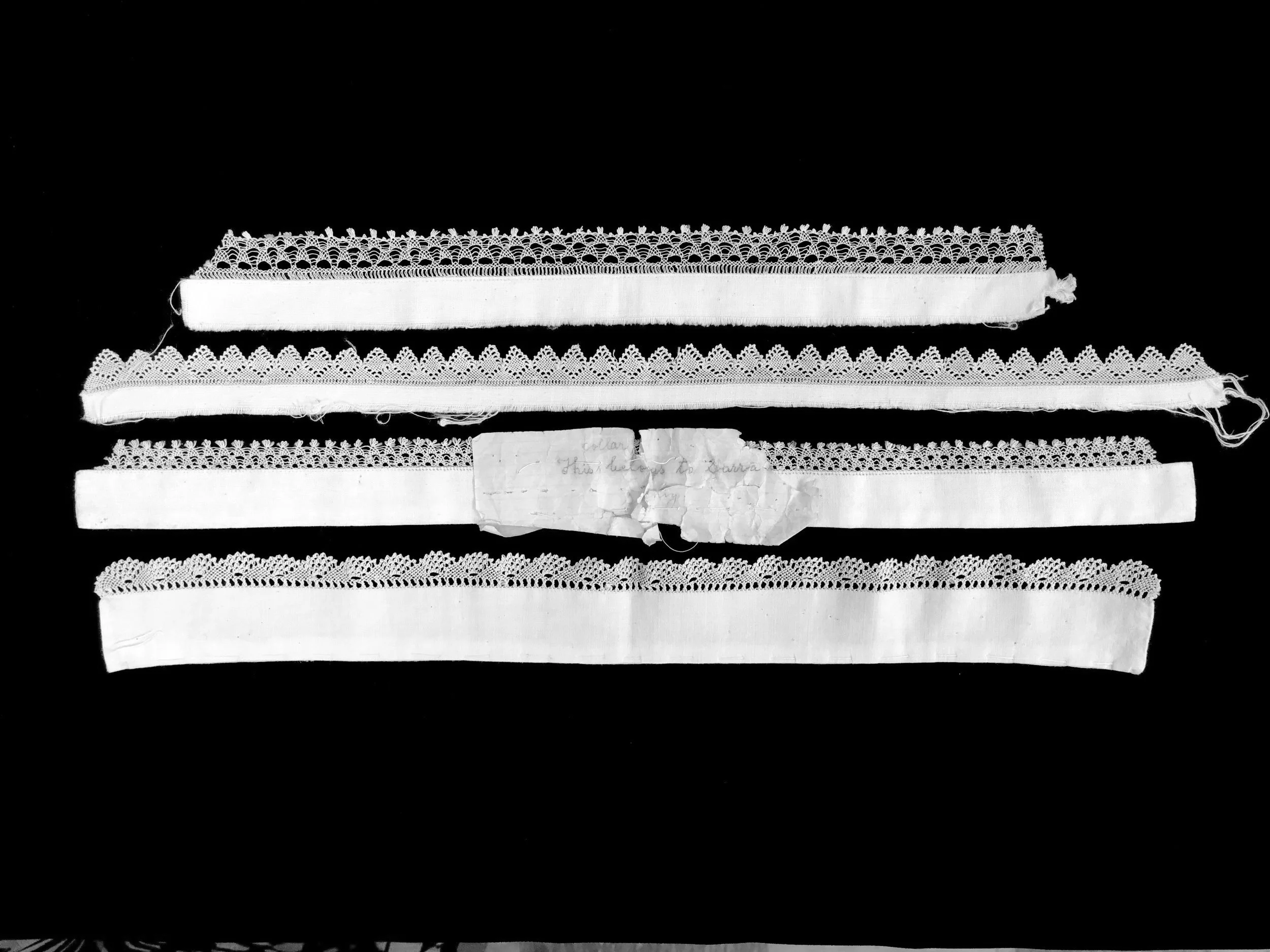 Black and white photo of four collars with Armenian needlelace trim and handwritten note stitched in