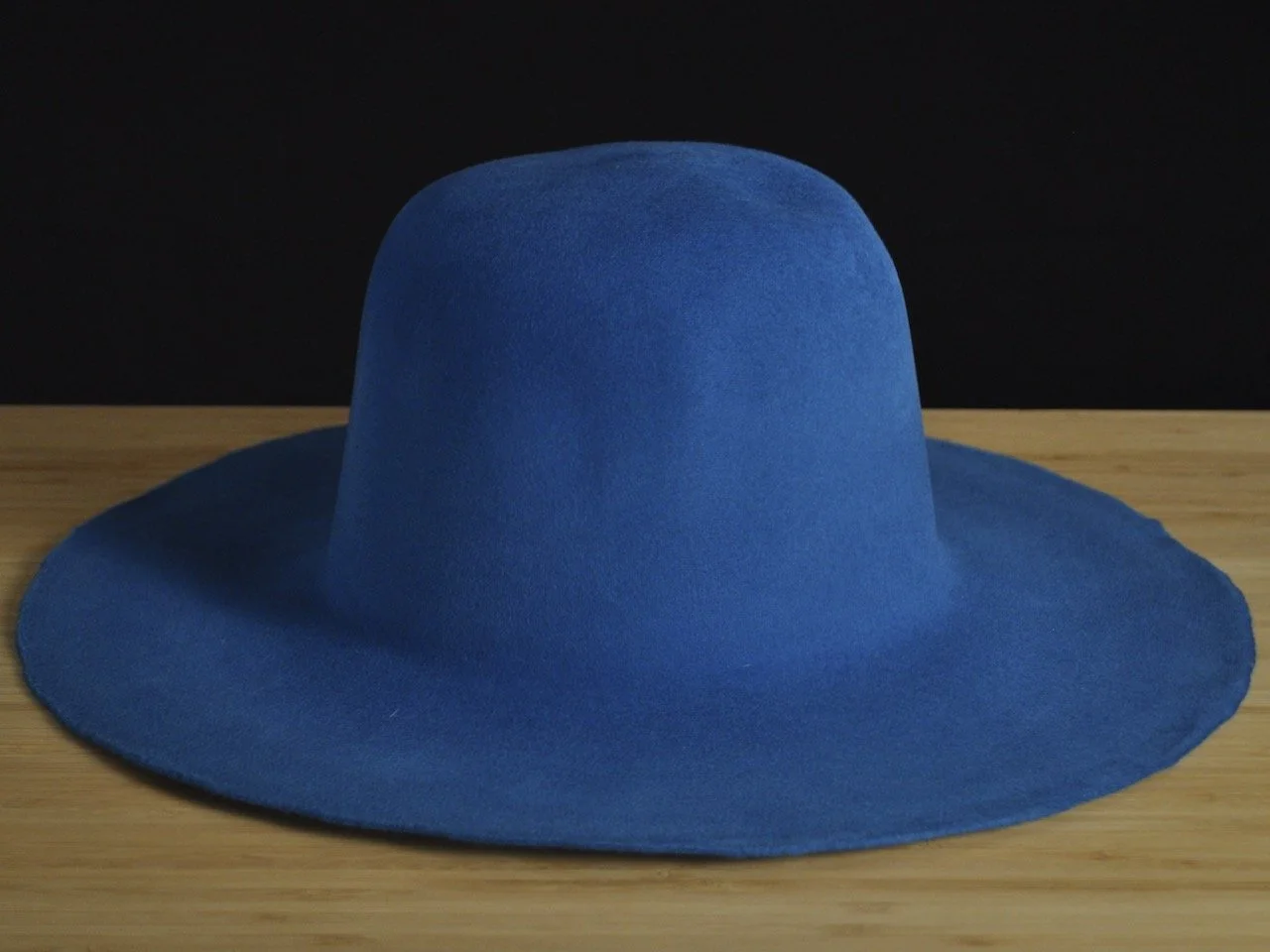 Cobalt blue wide-brimmed fur felt on a wooden surface against a black background.