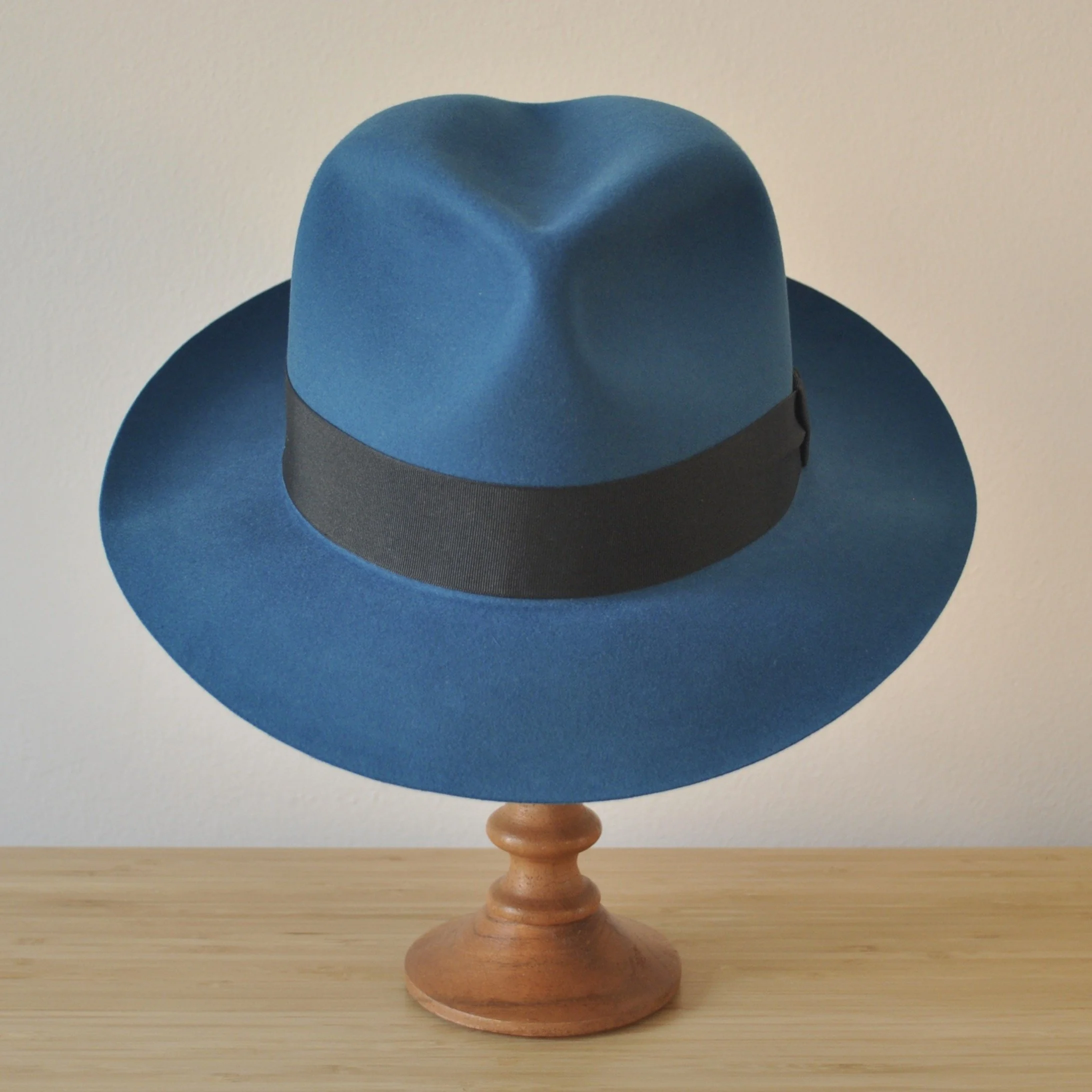 Front view of a cobalt blue felt fedora with a softly pinched centre dent crown, medium snap brim, and very dark blueish grey grosgrain ribbon with a modern tie (no bow).