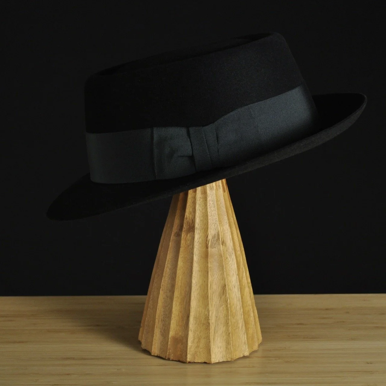 - Left view of The Midtowner black felt fedora with a clean tapered crown, medium snap brim, and matching black grosgrain ribbon with classic bow.