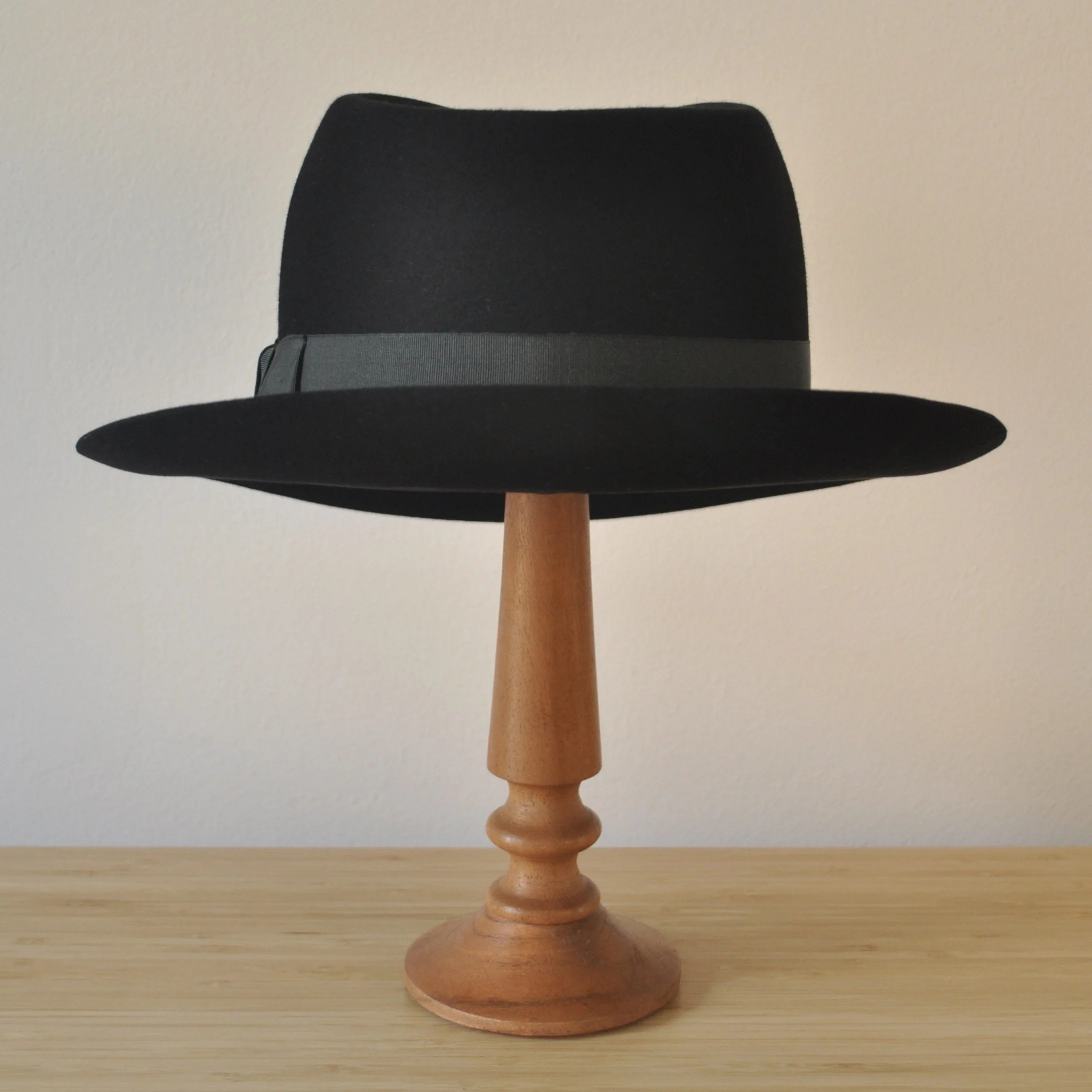 Back view of a black felt fedora with a clean structured crown, medium snap brim, and medium-dark bluish green grosgrain ribbon with classic bow.