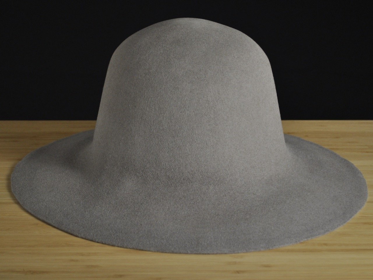 Gray wide-brimmed fur felt on a wooden surface with a black background.
