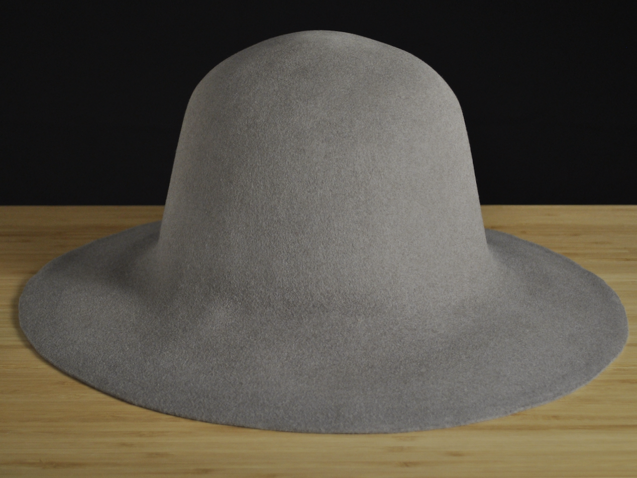 Sombrero de fieltro de pelo gris de ala ancha sobre una superficie de madera con fondo negro.