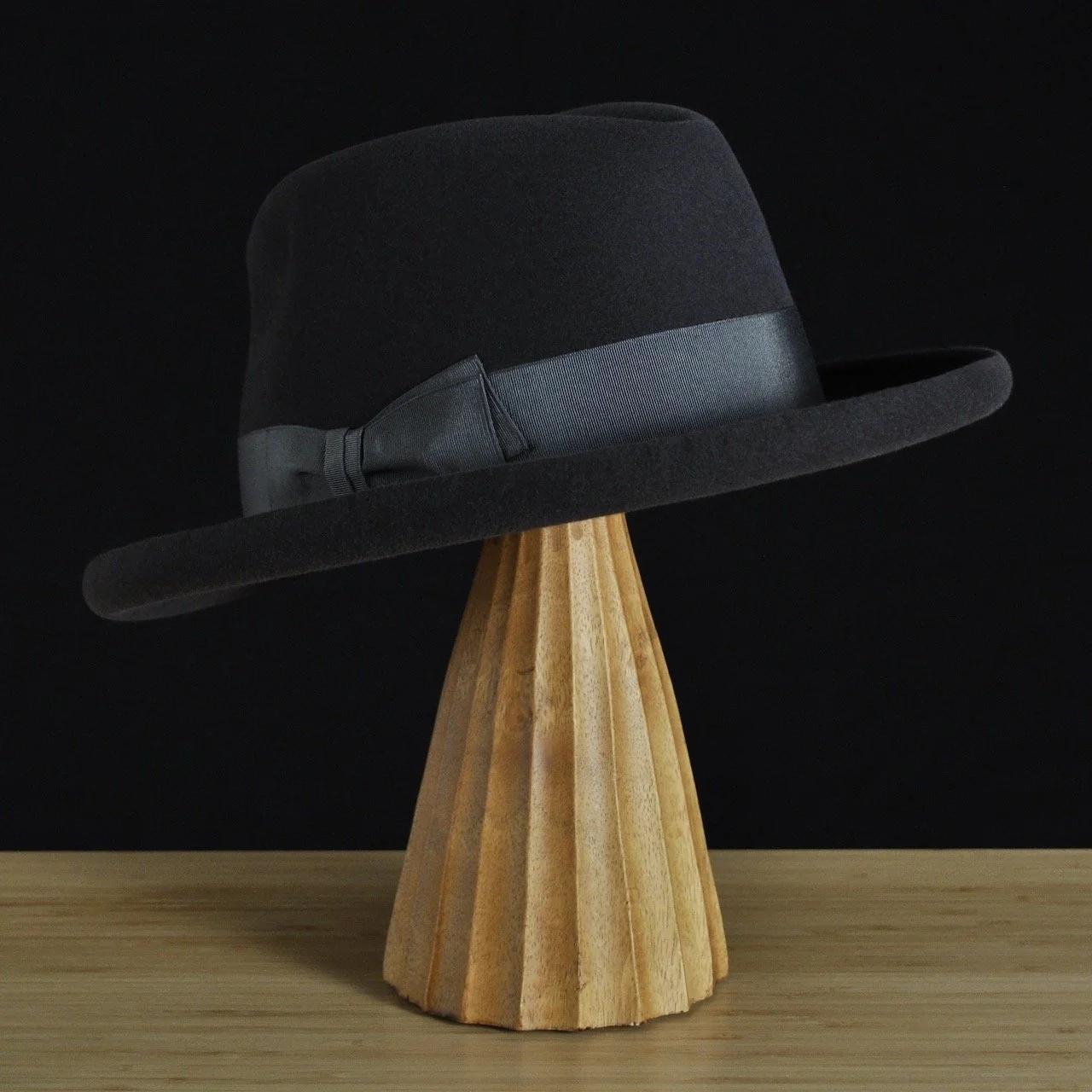 Vista de tres cuartos trasera izquierda del sombrero de fieltro antracita «The Westminster», con copa estructurada, ala rizada y cinta de grosgrain a juego con un clásico lazo doble.