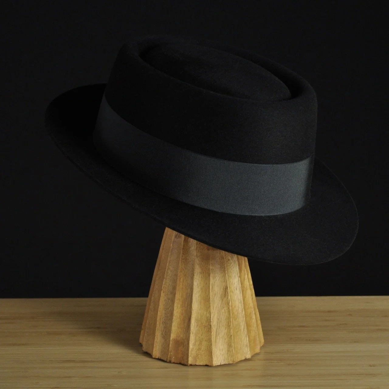 - Three-quarter front right view of The Midtowner black felt fedora with a clean tapered crown, medium snap brim, and matching black grosgrain ribbon with classic bow.