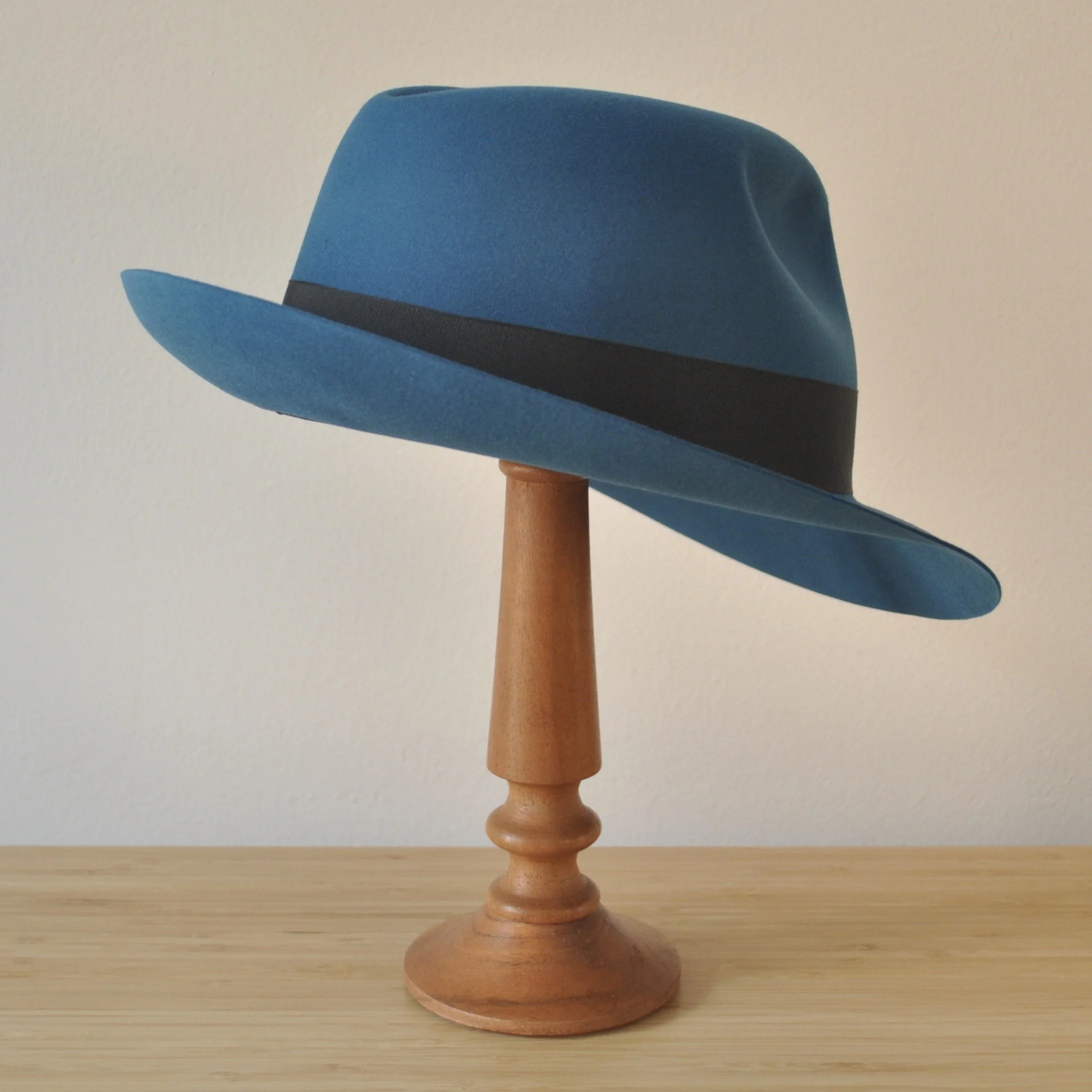 Three-quarter back right view of a cobalt blue felt fedora with a softly pinched centre dent crown, medium snap brim, and very dark blueish grey grosgrain ribbon with a modern tie (no bow).