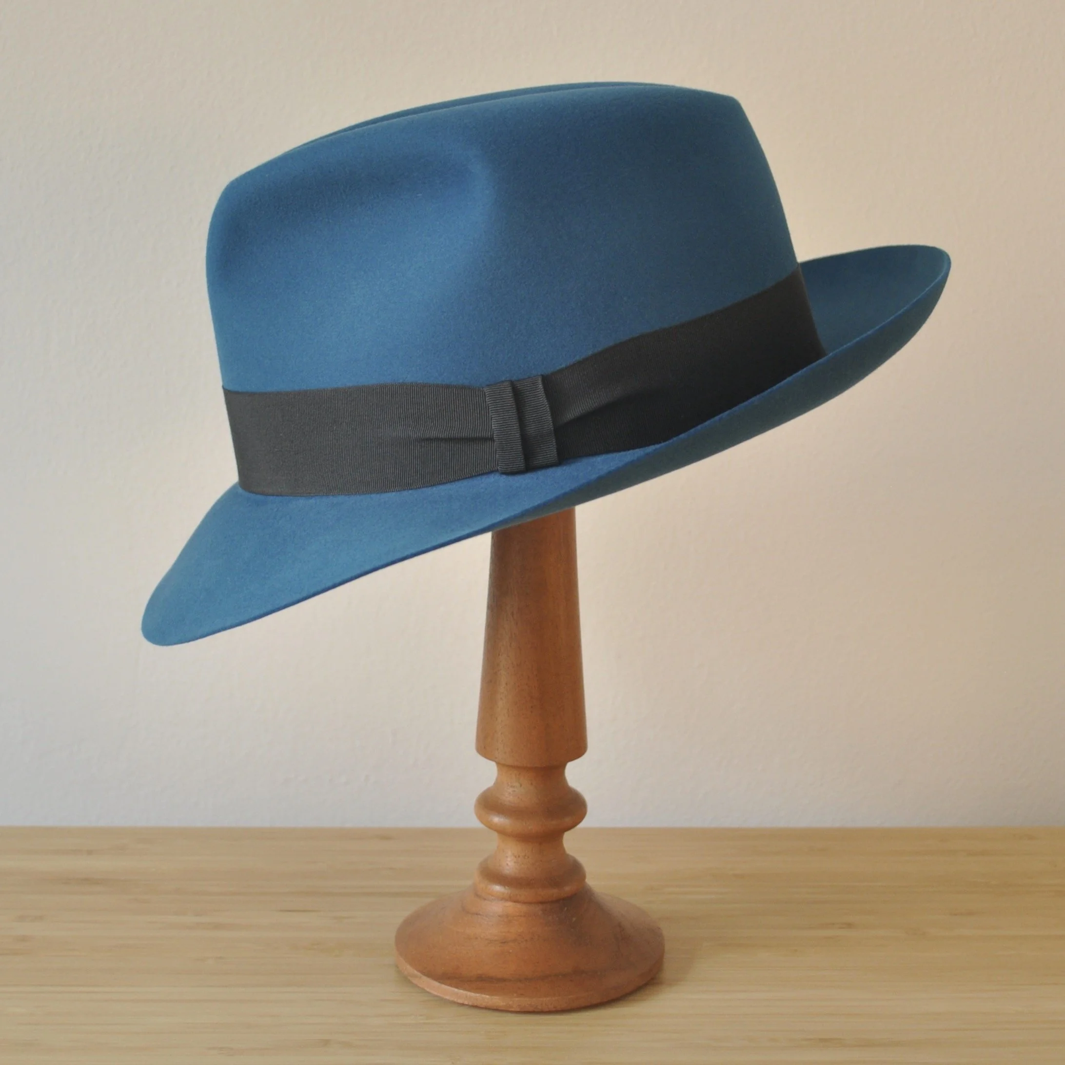 Left view of a cobalt blue felt fedora with a softly pinched centre dent crown, medium snap brim, and very dark blueish grey grosgrain ribbon with a modern tie (no bow).
