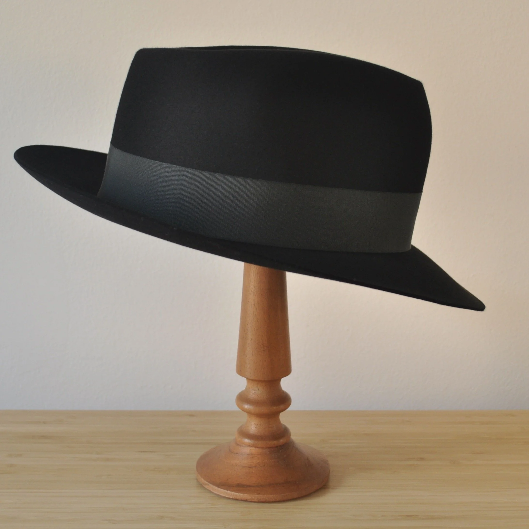 Right side view of a black felt fedora with a clean structured crown, medium snap brim, and medium-dark bluish green grosgrain ribbon with classic bow.