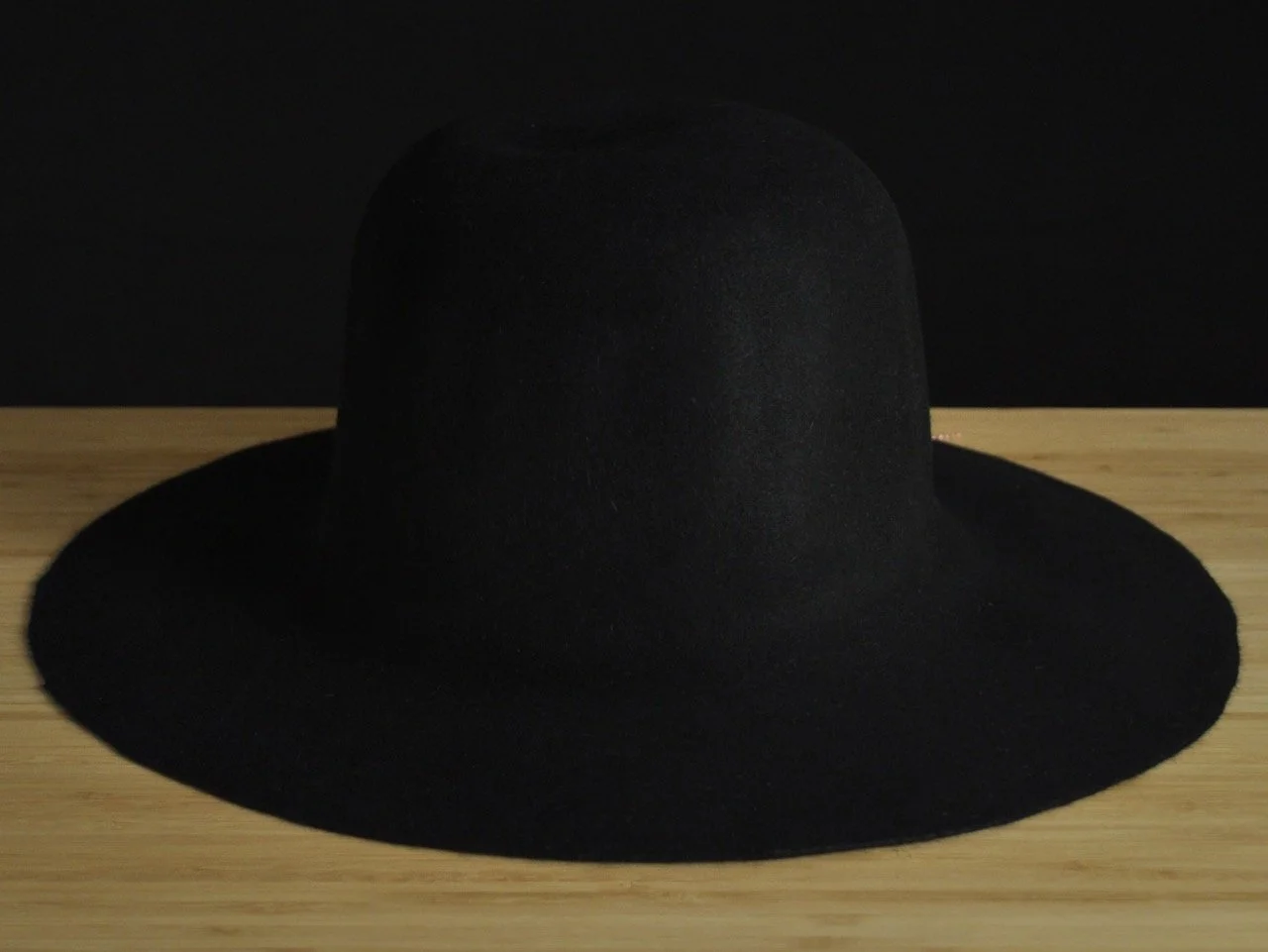 Noir wide-brimmed fur felt positioned on a wooden surface against a black background.