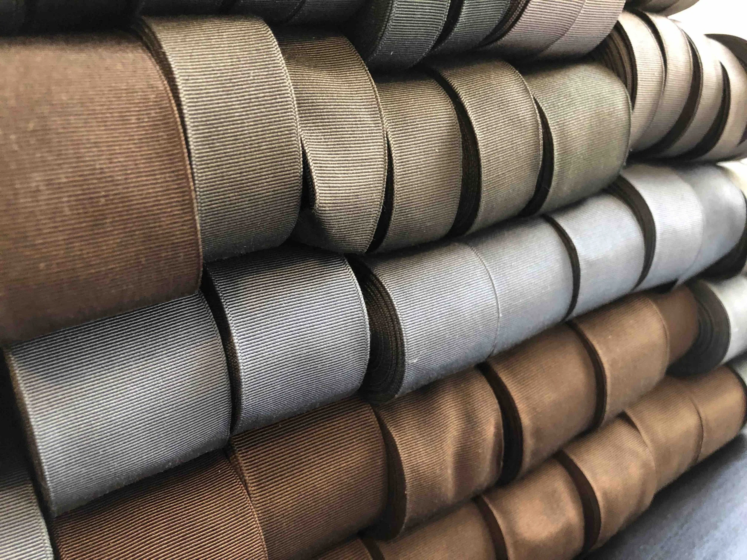 Rollos de cinta de grosgrain francesa en varios tonos de marrón, gris y beige, apilados.