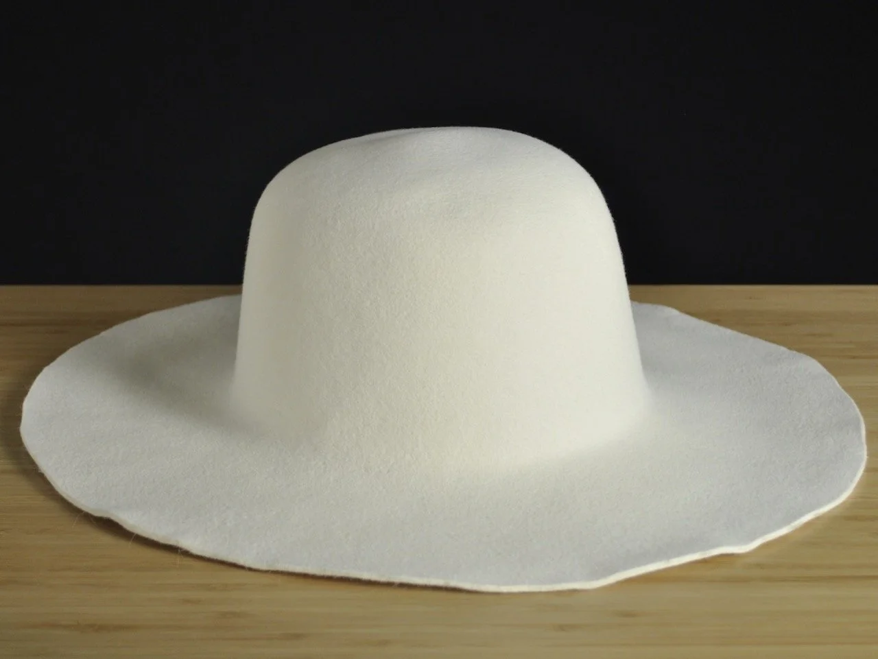 White wide-brimmed fur felt, placed on a wooden surface with a dark background.