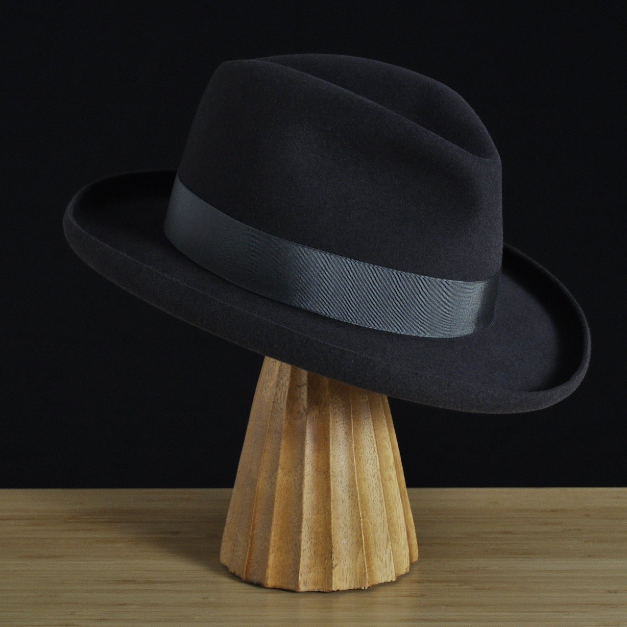 Vista frontal a tres cuartos del sombrero de fieltro antracita «The Westminster», con copa estructurada, ala rizada y cinta de grosgrain a juego con un clásico lazo doble.