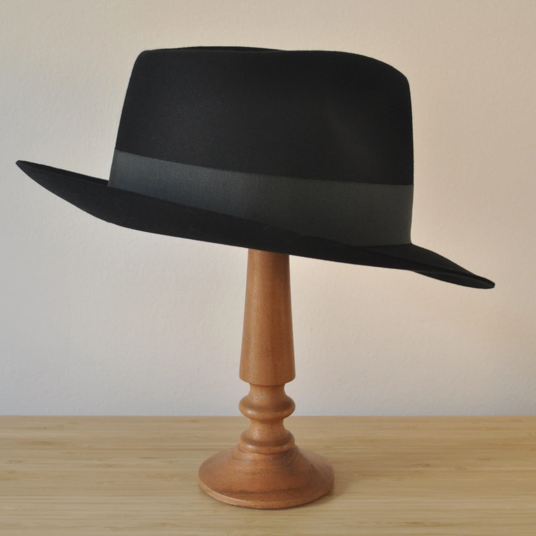 Three-quarter back right view of a black felt fedora with a clean structured crown, medium snap brim, and medium-dark bluish green grosgrain ribbon with classic bow.