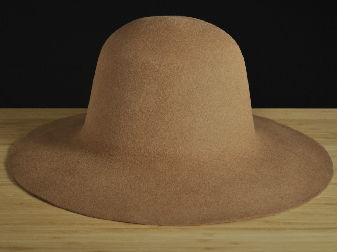 Sombrero de fieltro de pelo de color beige y ala ancha sobre una superficie de madera con fondo negro.