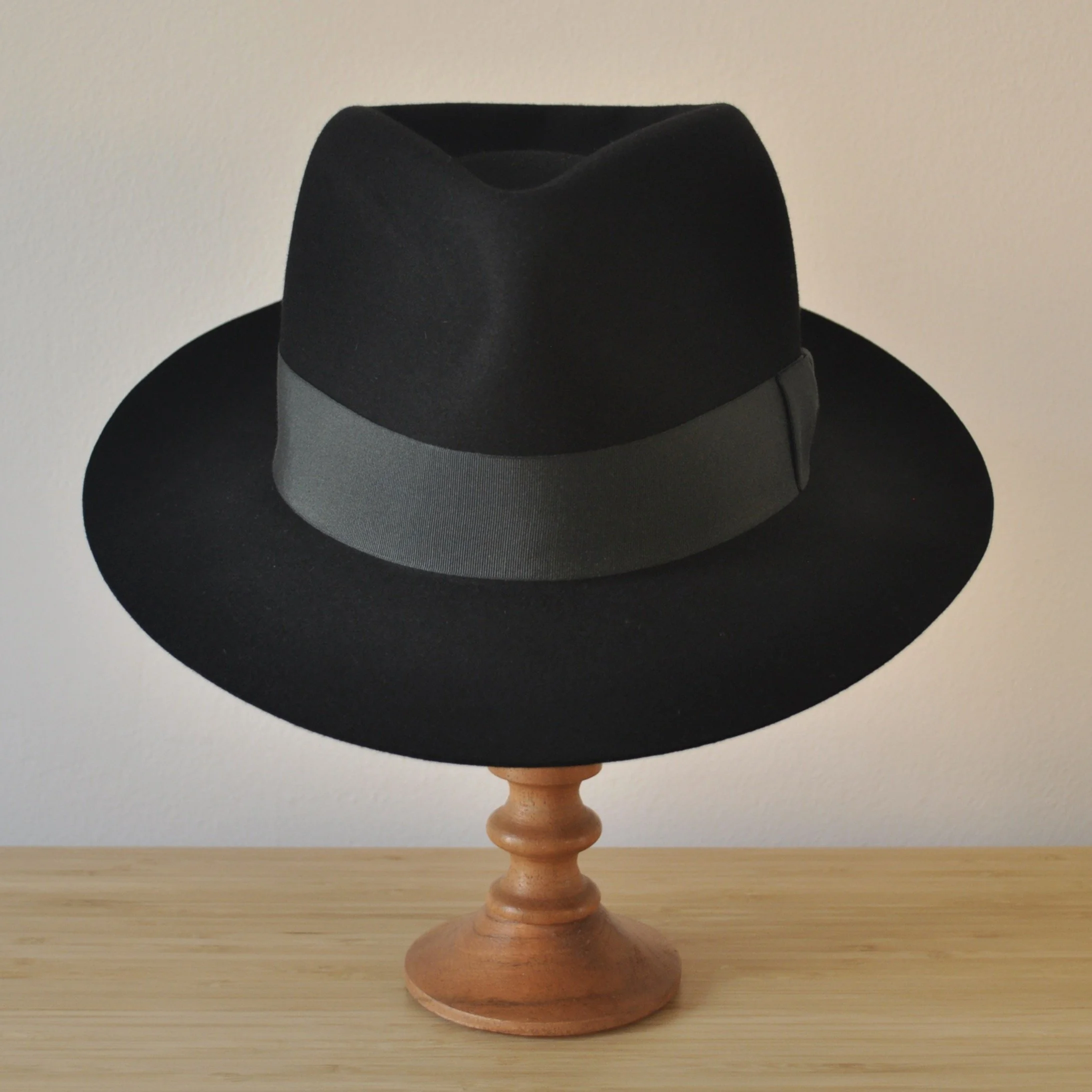 Front view of a black felt fedora with a clean structured crown, medium snap brim, and medium-dark bluish green grosgrain ribbon with classic bow.
