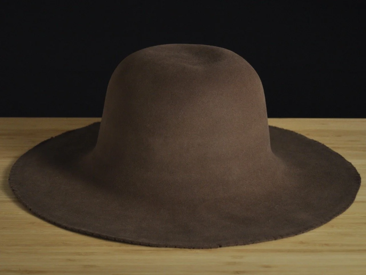 Brown wide-brimmed fur felt on a wooden surface against a dark background.
