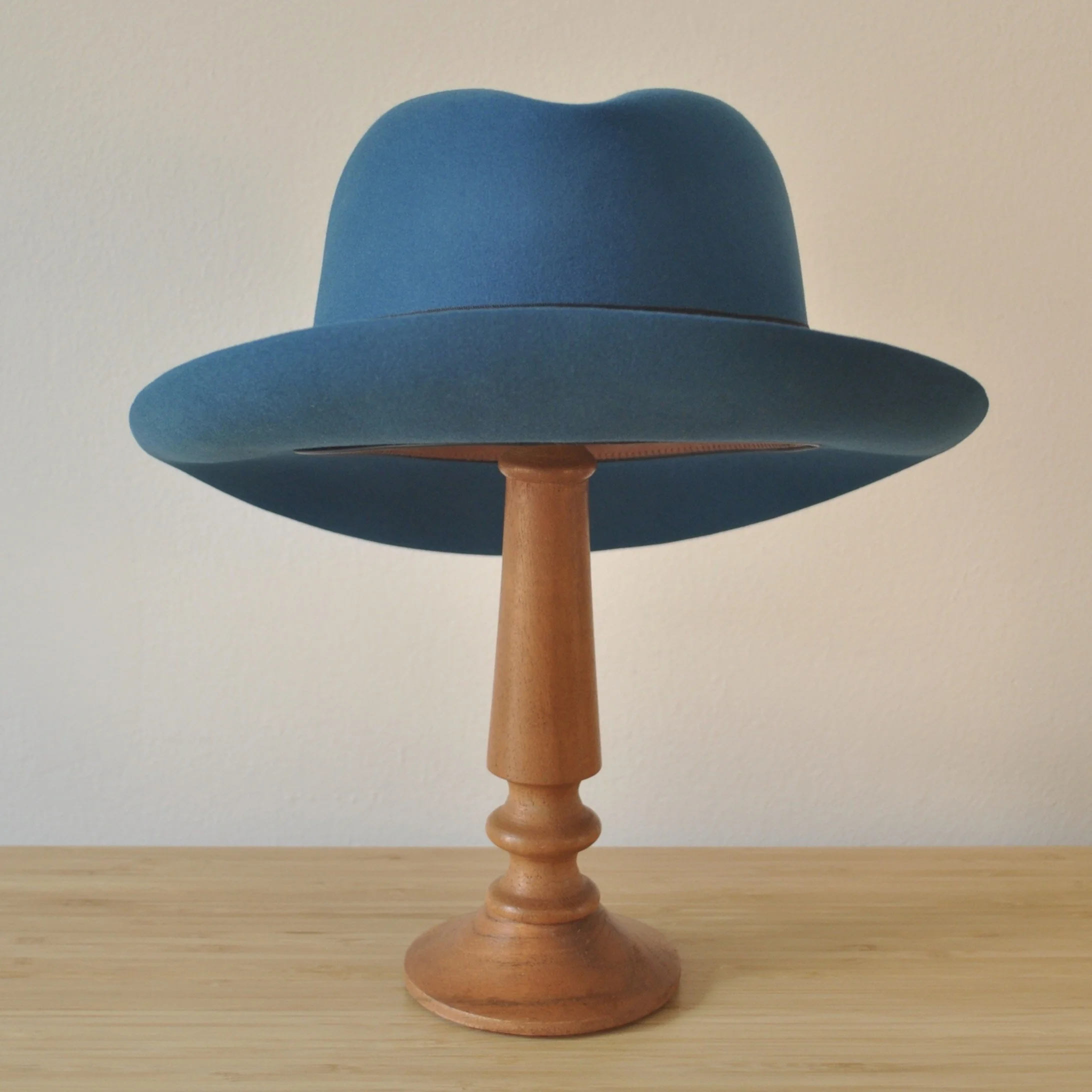 Back view of a cobalt blue felt fedora with a softly pinched centre dent crown, medium snap brim, and very dark blueish grey grosgrain ribbon with a modern tie (no bow).