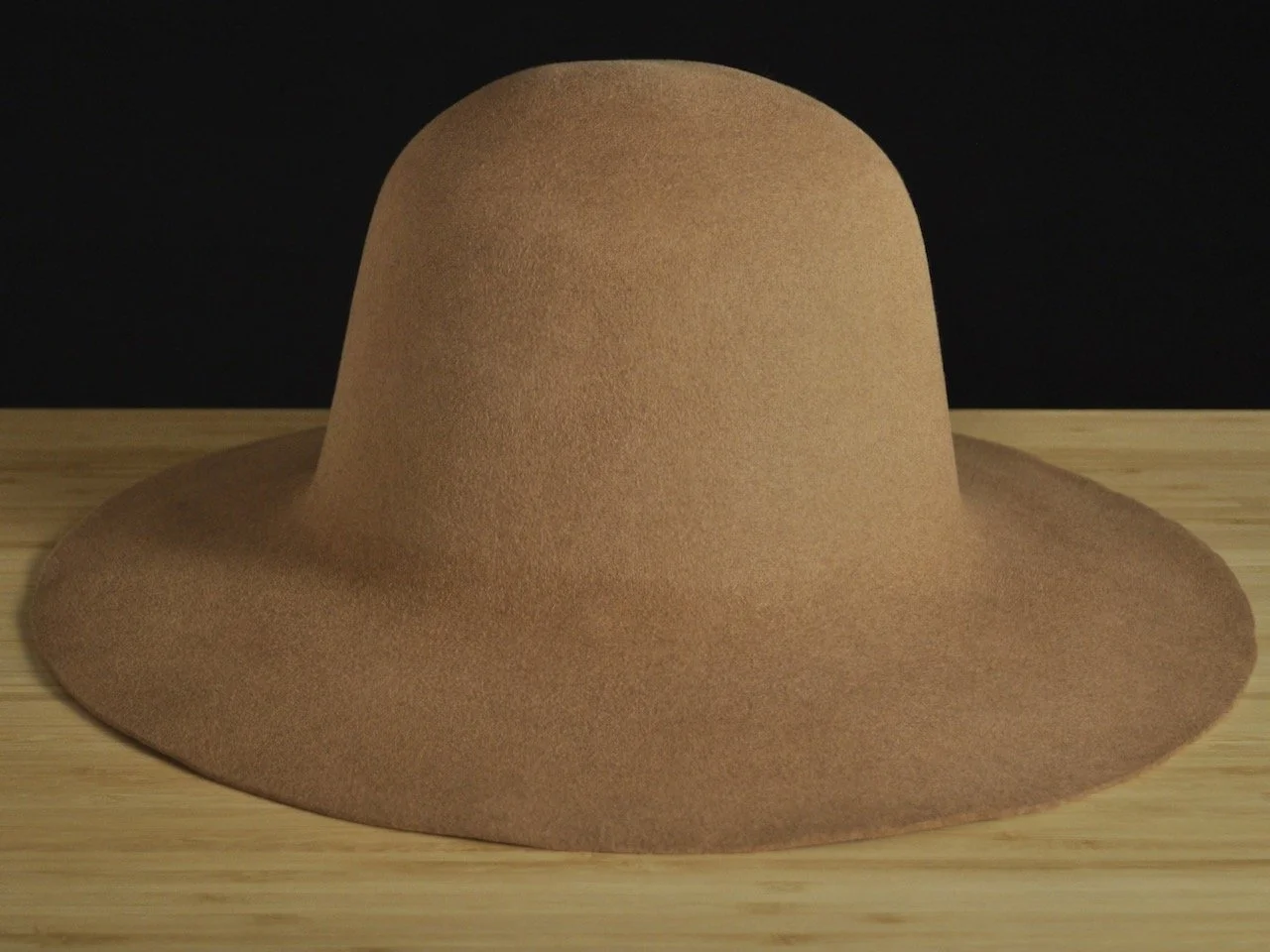 Tan wide-brimmed fur felt hat on a wooden surface with a black background.
