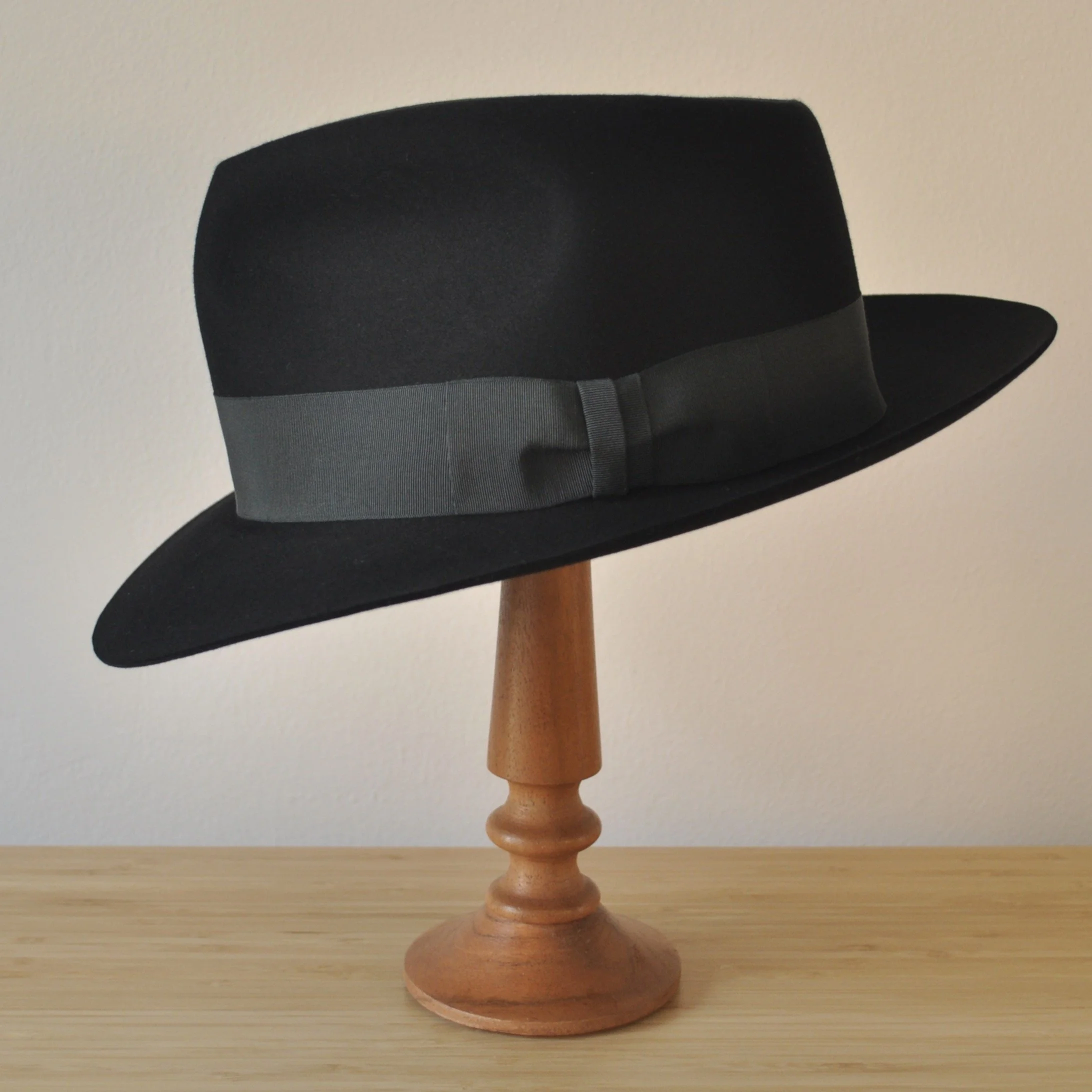 Left side view of a black felt fedora with a clean structured crown, medium snap brim, and medium-dark bluish green grosgrain ribbon with classic bow.