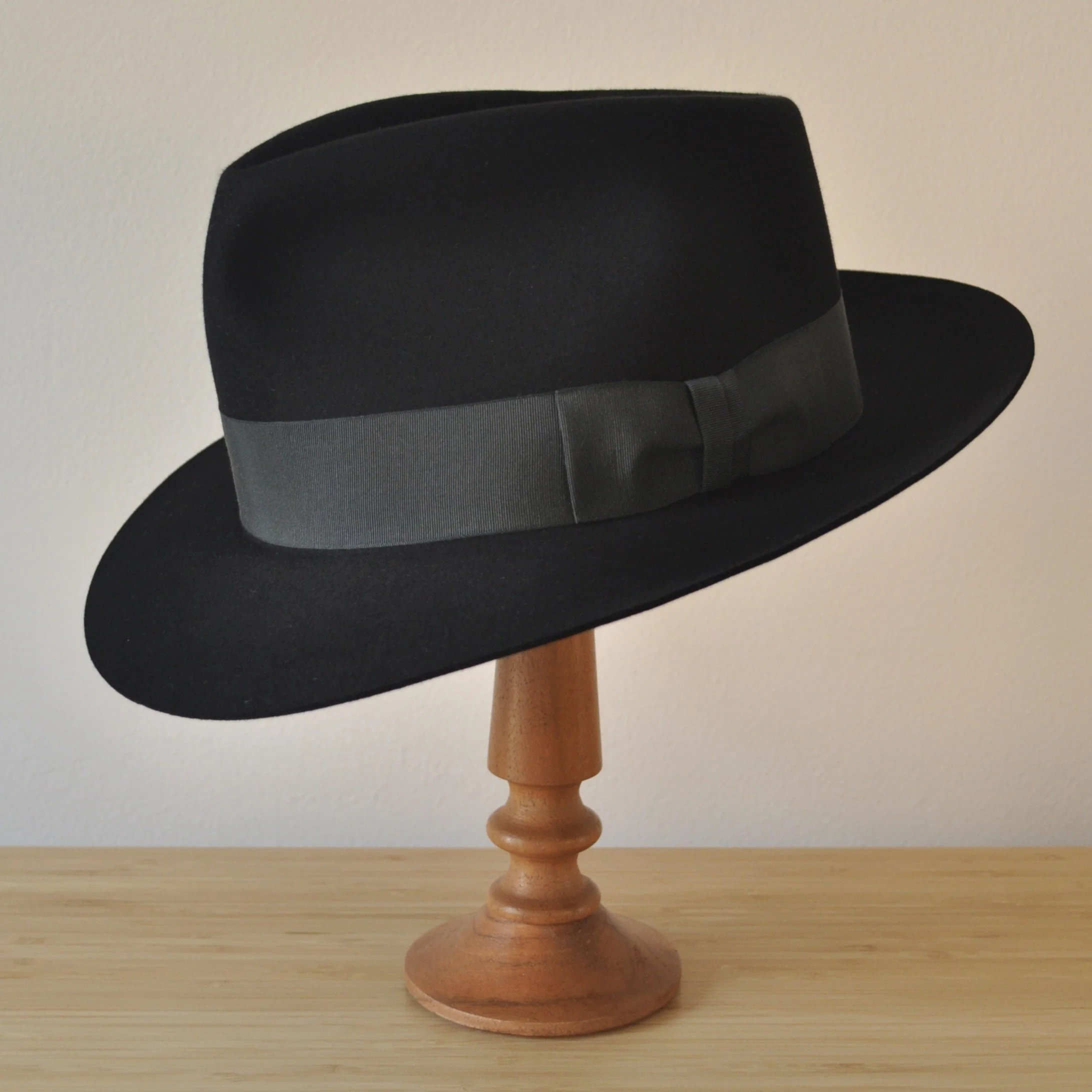 Three-quarter front left view of a black felt fedora with a clean structured crown, medium snap brim, and medium-dark bluish green grosgrain ribbon with classic bow.