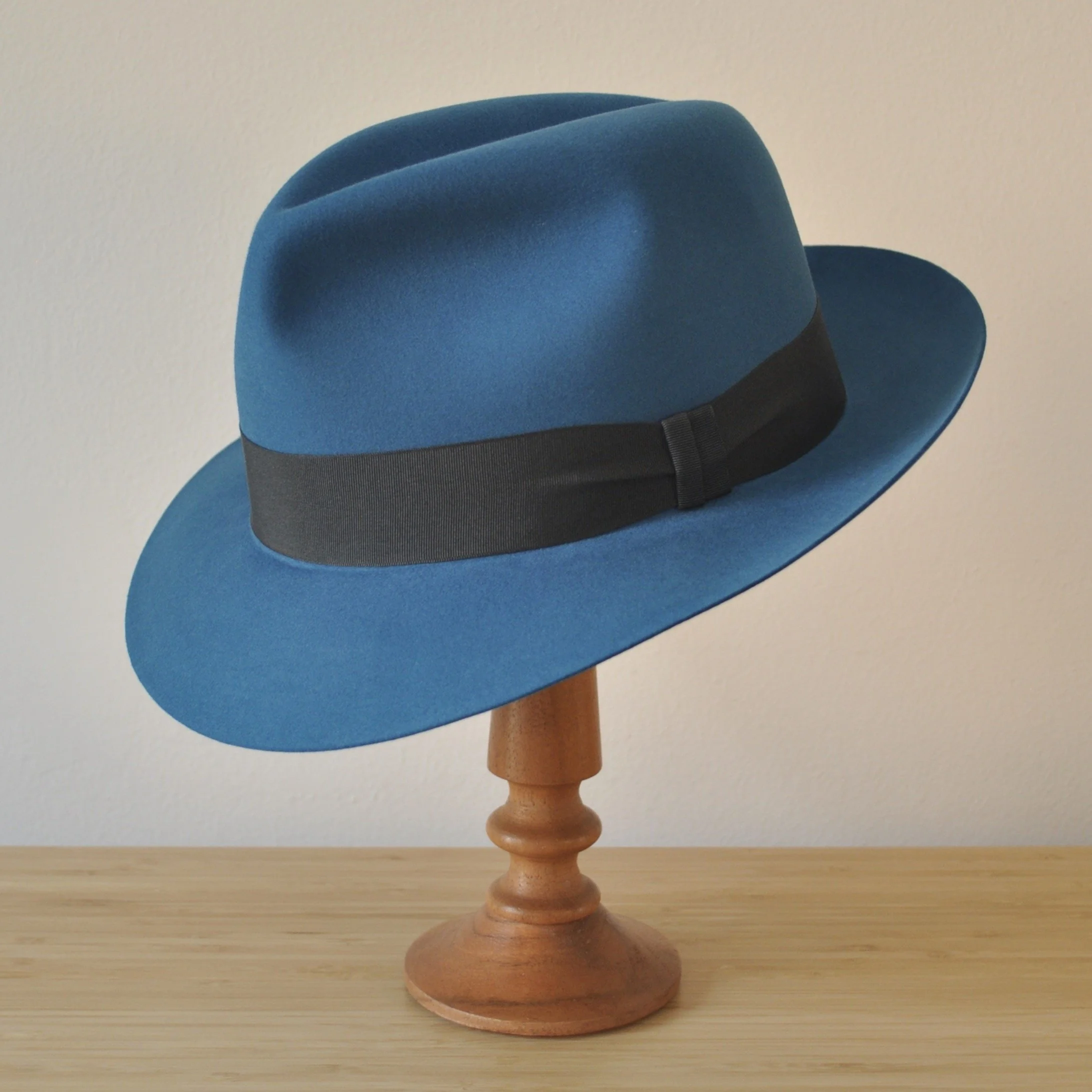 Three-quarter front left view of a cobalt blue felt fedora with a softly pinched centre dent crown, medium snap brim, and very dark blueish grey grosgrain ribbon with a modern tie (no bow).