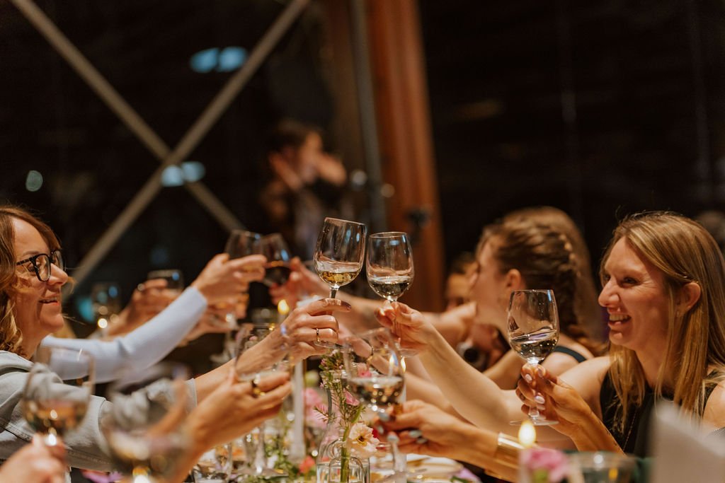 Women at a dinner party raising wine glasses in a toast, smiling and enjoying the celebration indoors.
