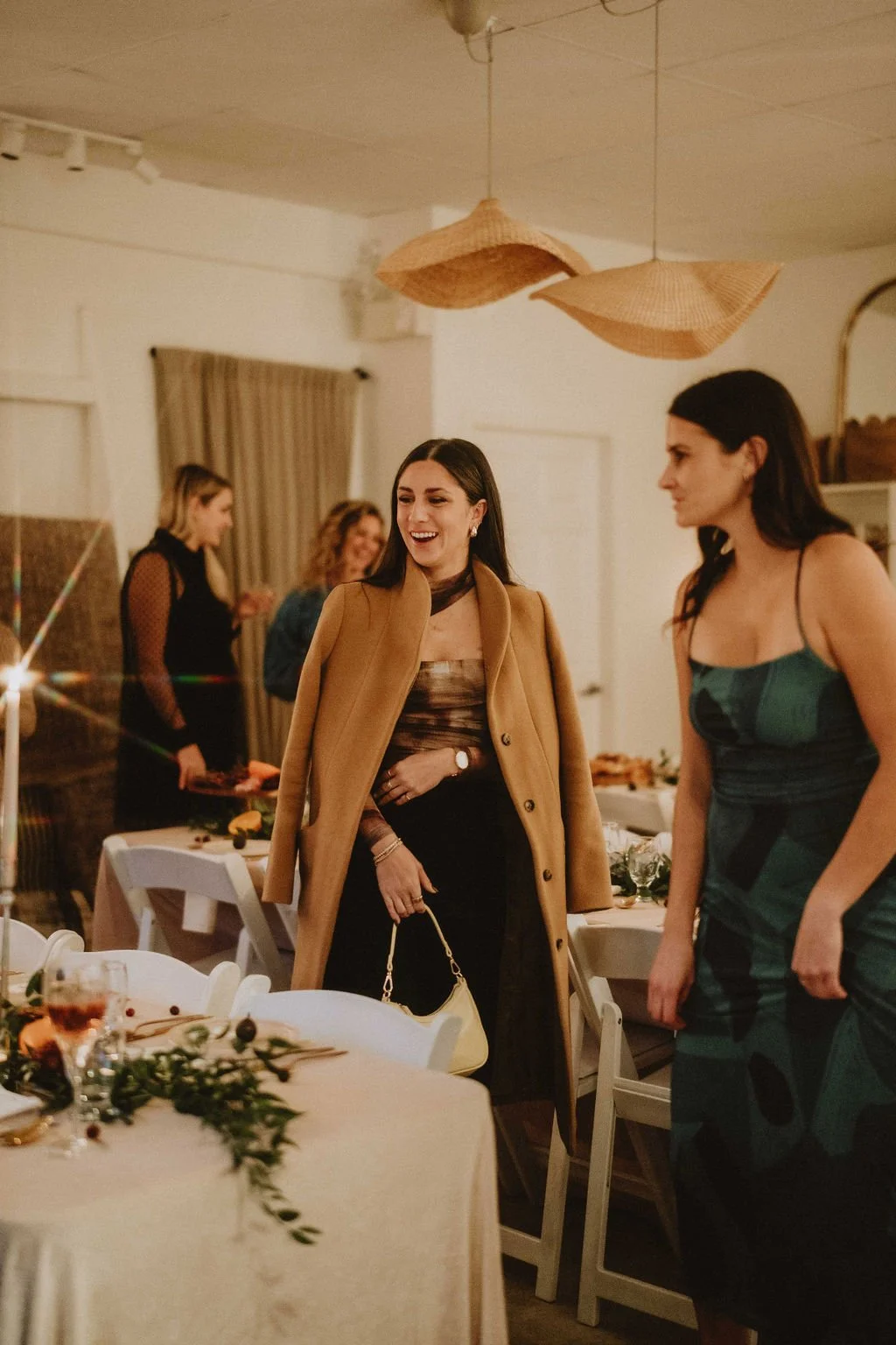 People at a dinner party, with women talking and laughing, decorated dining table, warm lighting and modern decor.