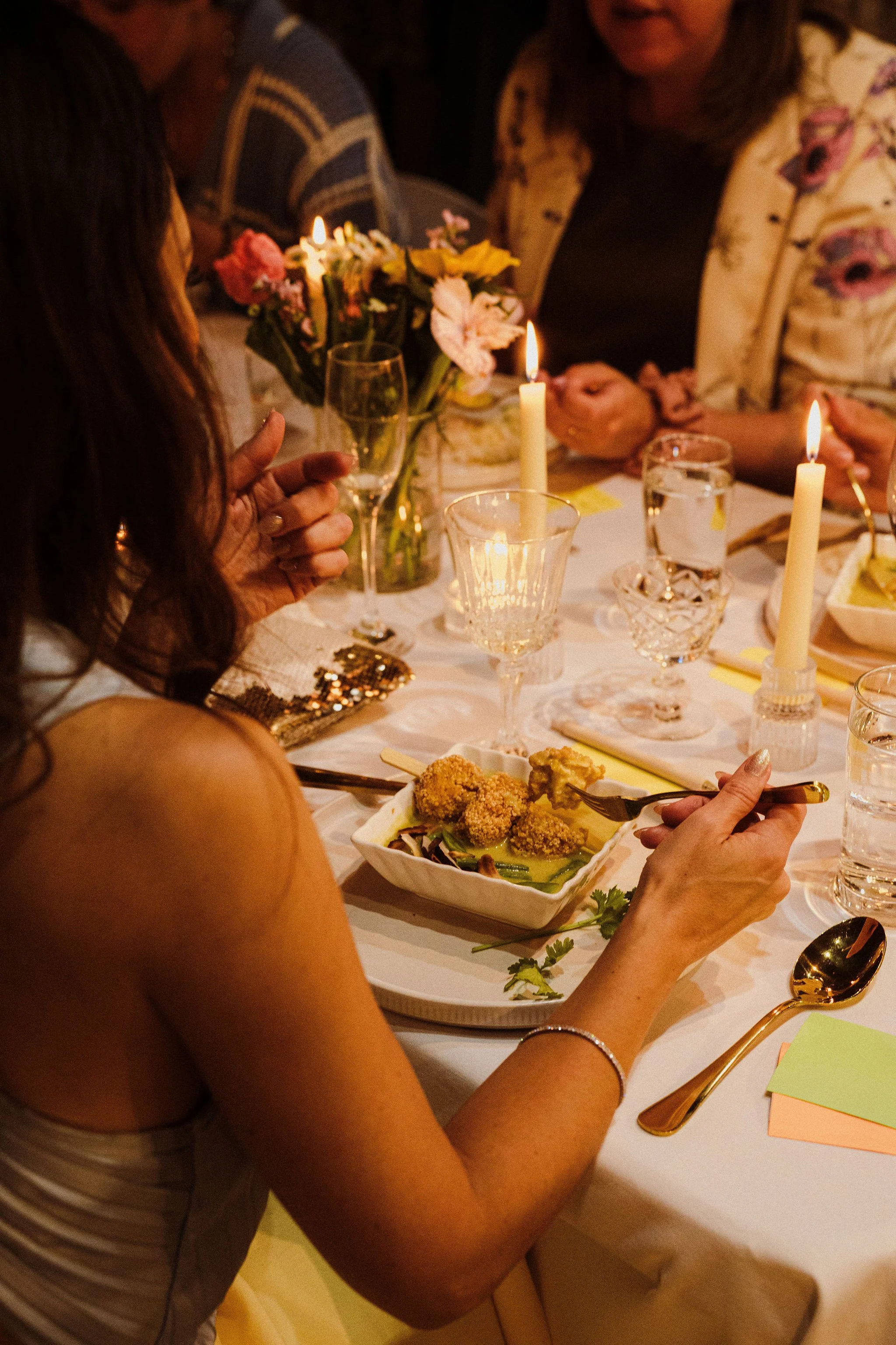 People gathered at a dinner table with candles, flowers, and glassware, enjoying a meal.