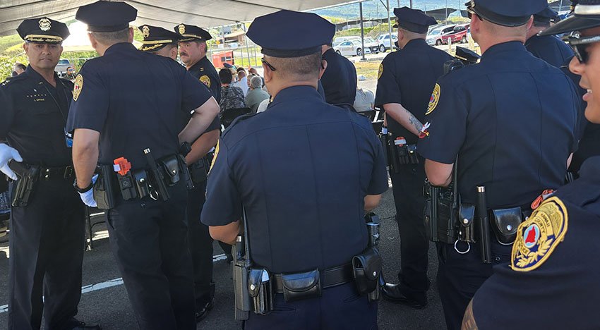 Group of police officers in uniform standing and talking outside under a tent.