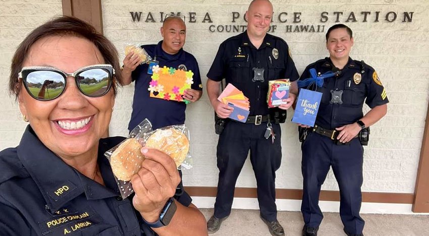 Four police officers in uniform smiling outside Waimea Police Station in Hawaii, holding thank you notes and gift bags.