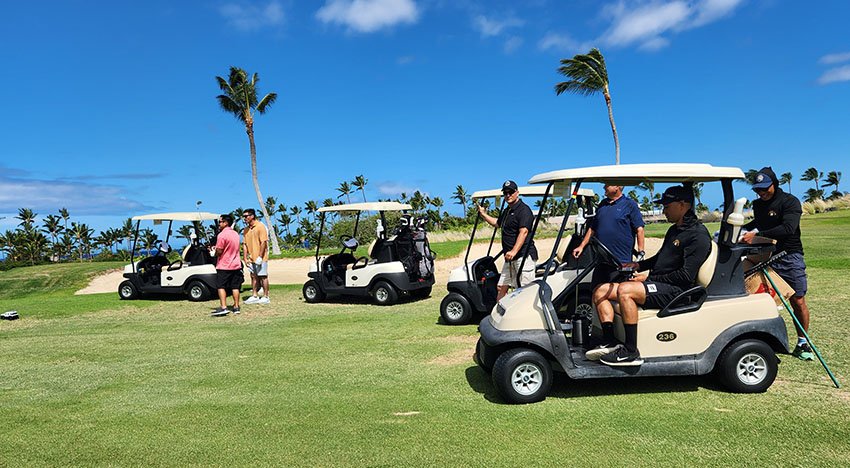 Group of people with golf carts on a golf course with palm trees under a blue sky.